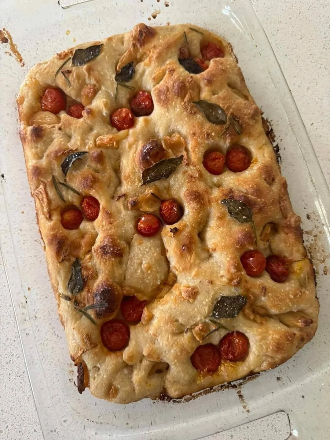 Baked flatbread topped with cherry tomatoes, basil leaves, and melted cheese in a glass baking dish.