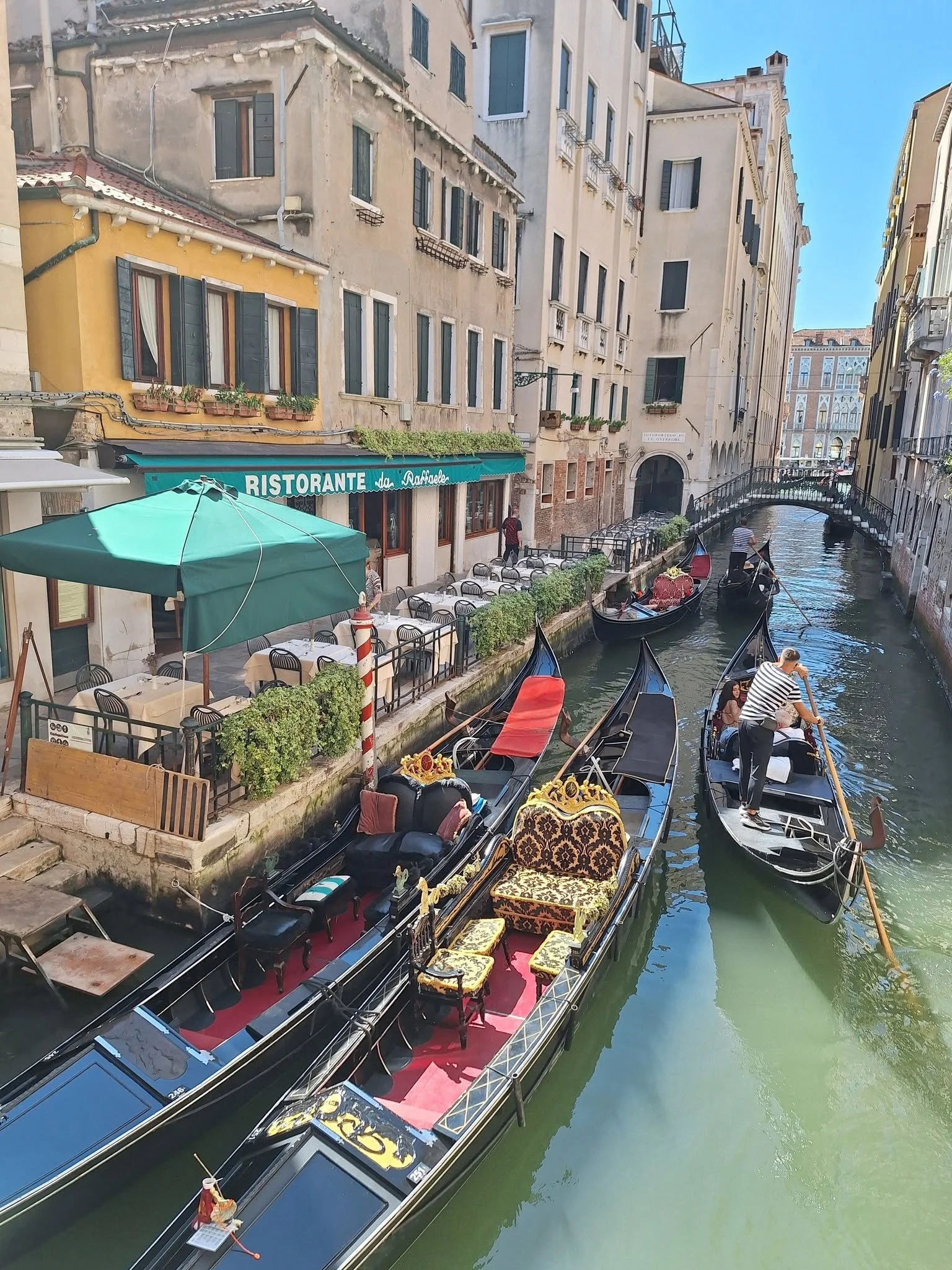 Gondolas on a canal in Venice, Italy, with buildings lining the waterway and a person steering a gondola, scenic city view.