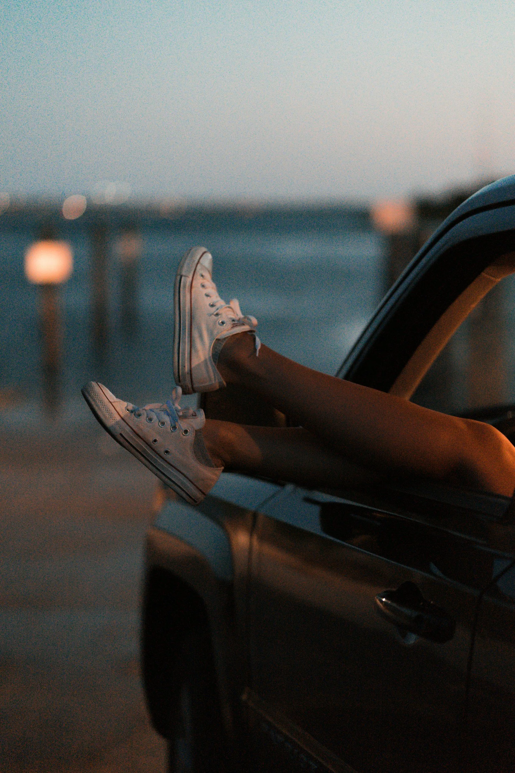 De afbeelding toont een persoon die in de auto ligt met de benen uit het raam en witte sneakers aan.