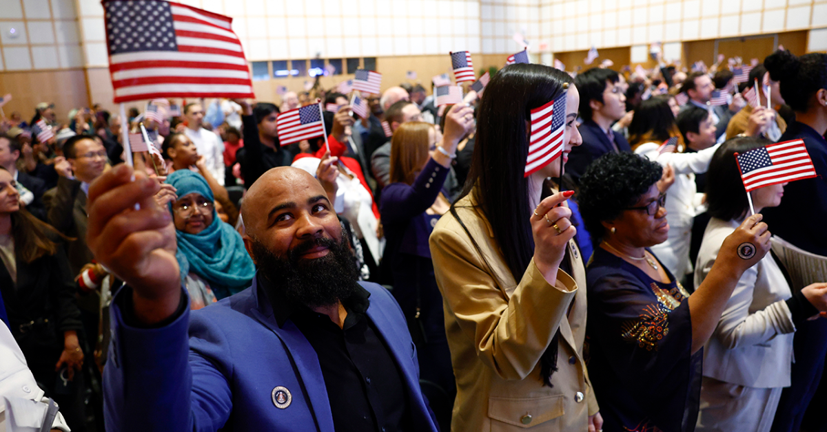 Large crowd of people at a patriotic event, holding small American flags and a large American flag in the background.