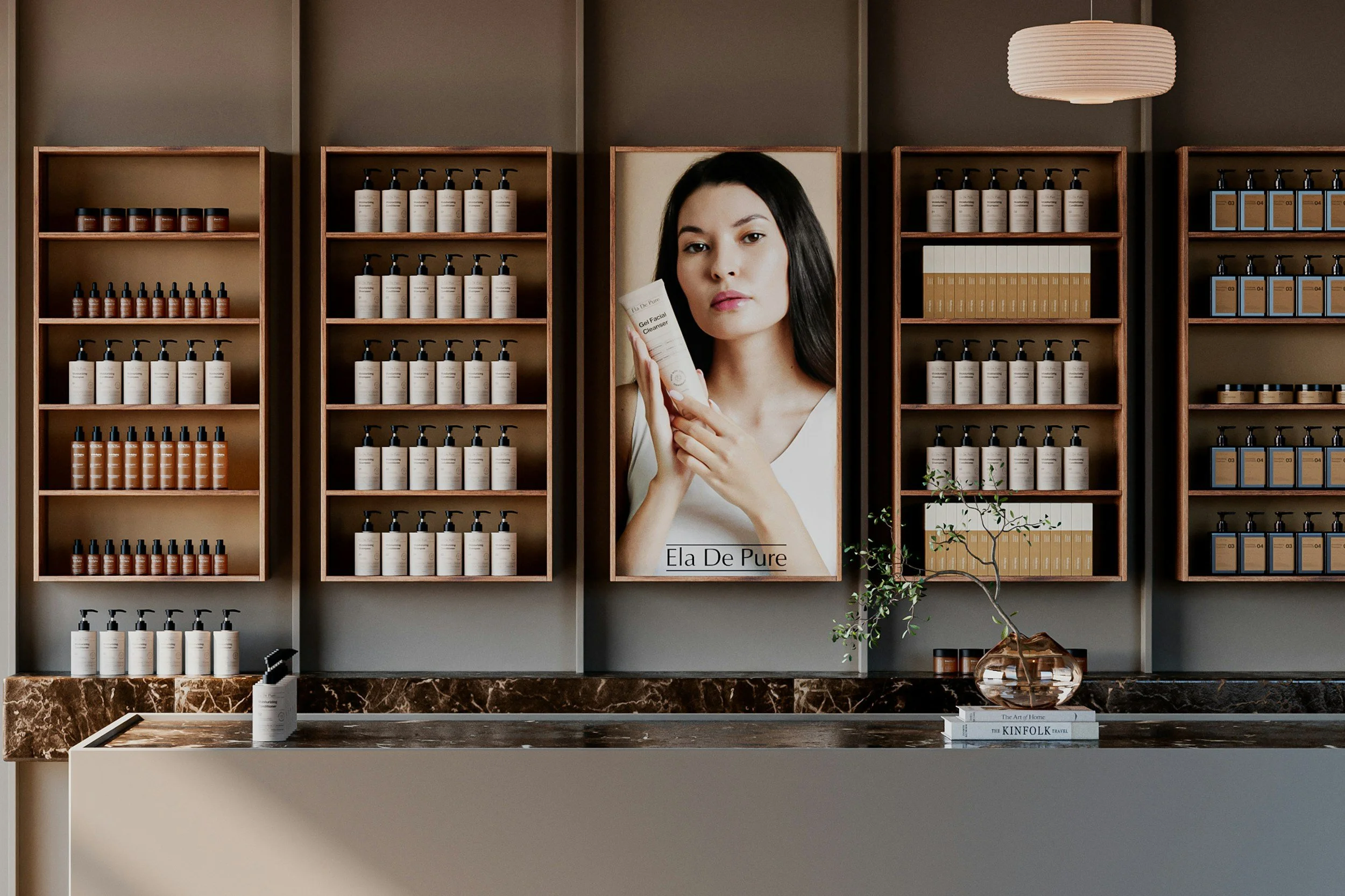 Interior of a skincare or beauty product store with wooden shelves filled with bottles and containers. A large poster of a woman holding a facial cleanser is mounted on the wall. There is a marble counter with a pump bottle and a small potted plant, and books titled 'The Art of Home' and 'The KINFOLK Travel' are placed on the counter.