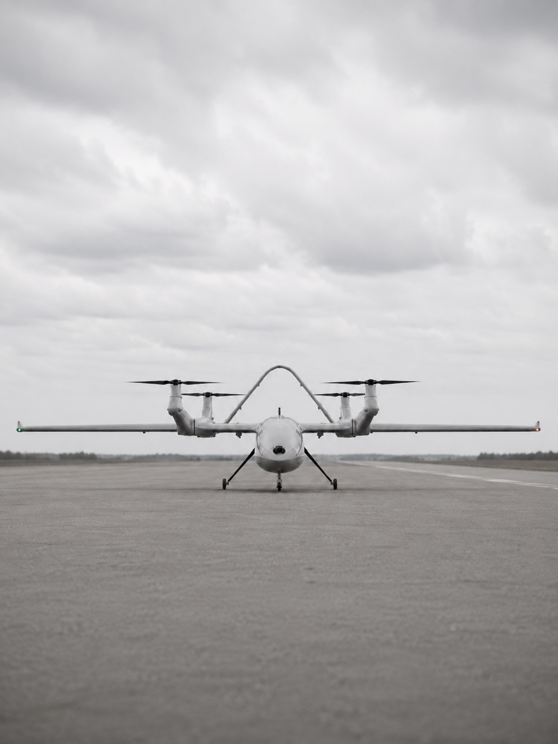 A front view of a futuristic aircraft on an empty runway with a cloudy sky in the background.
