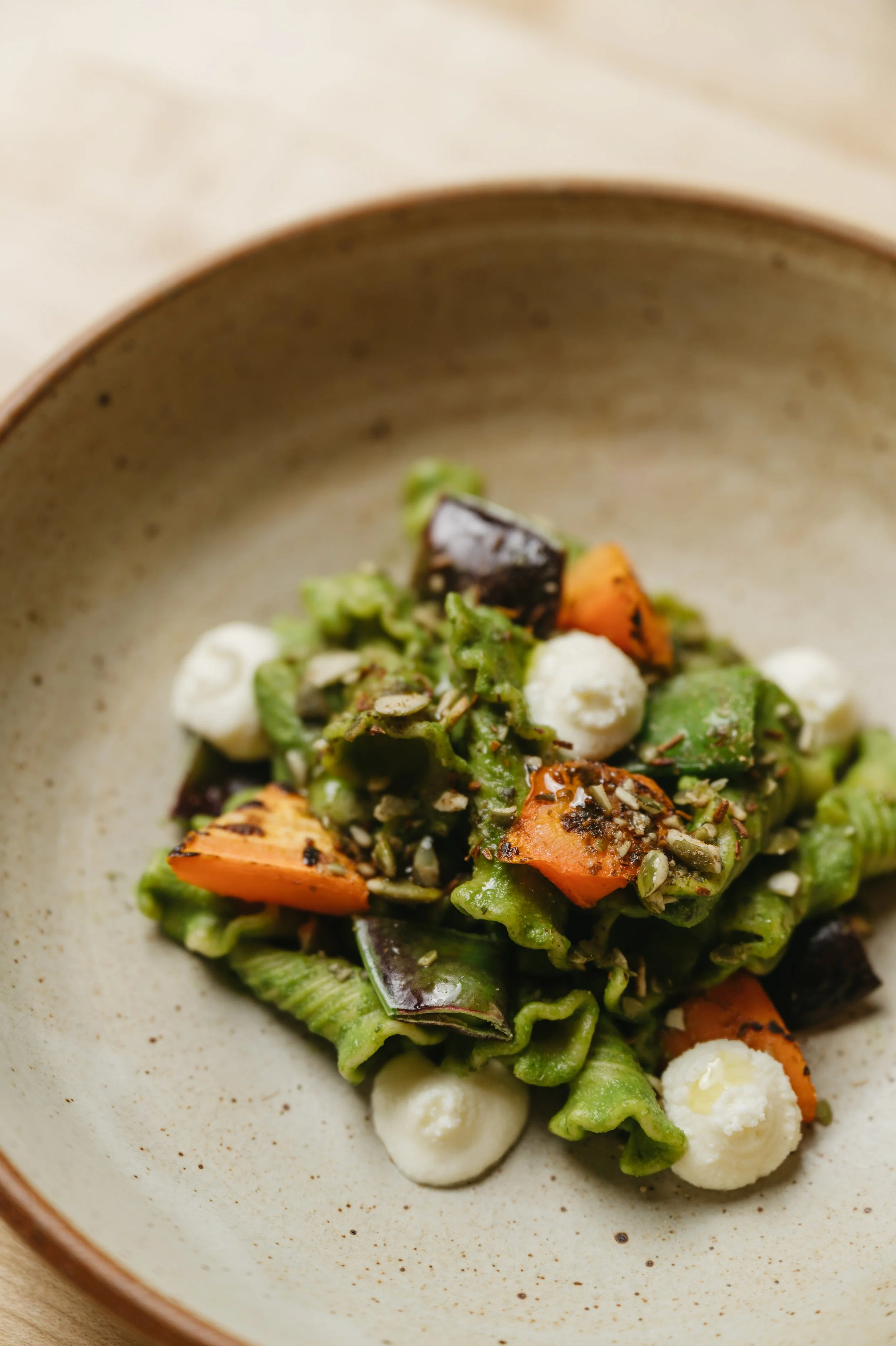 Close-up of a bowl with roasted or grilled vegetables, including carrots, zucchini, and eggplant, garnished with herbs and accompanied by small dollops of cheese or cream.