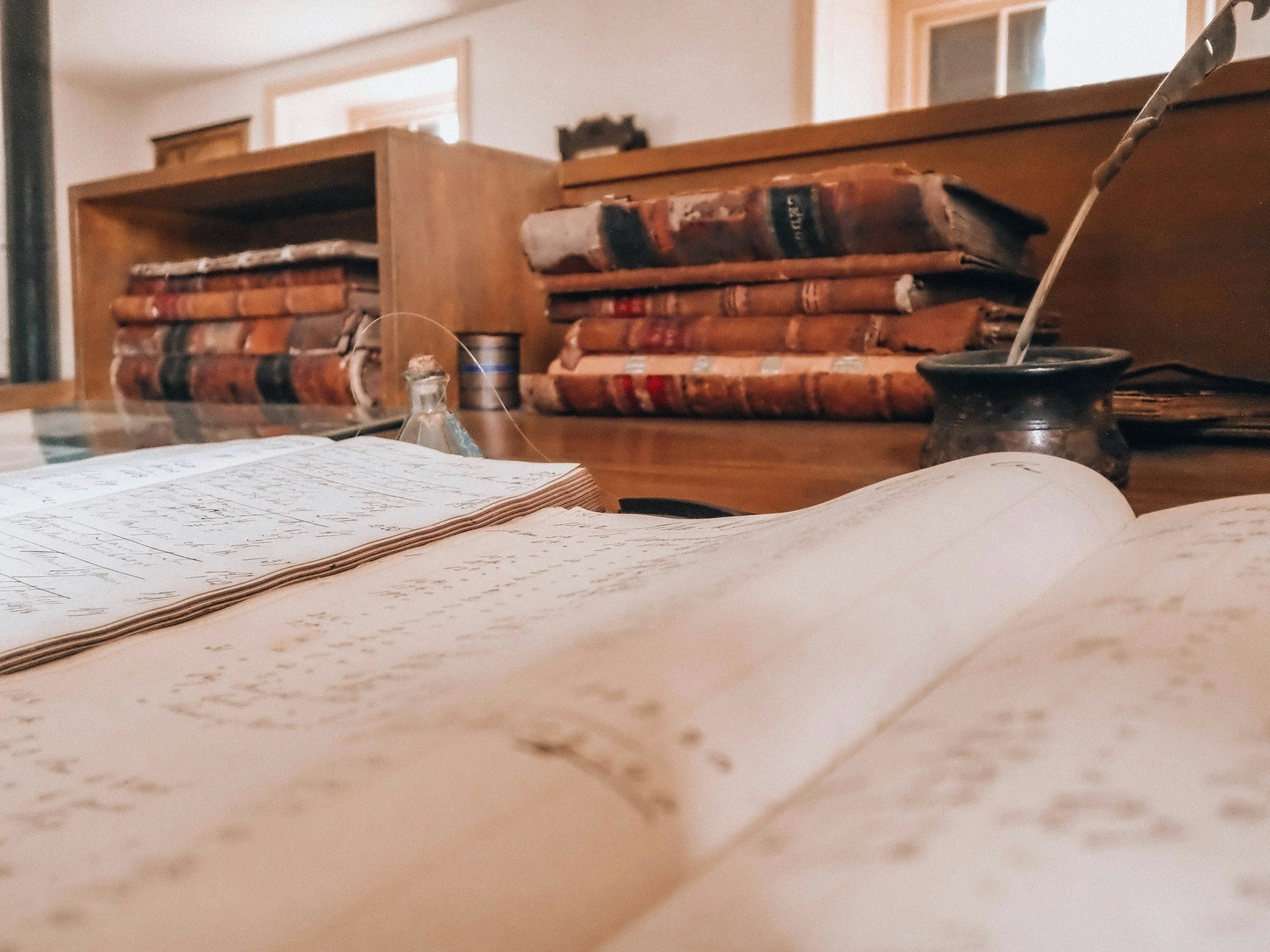 Old, worn books stacked on a wooden desk with handwritten notes and papers in the foreground.