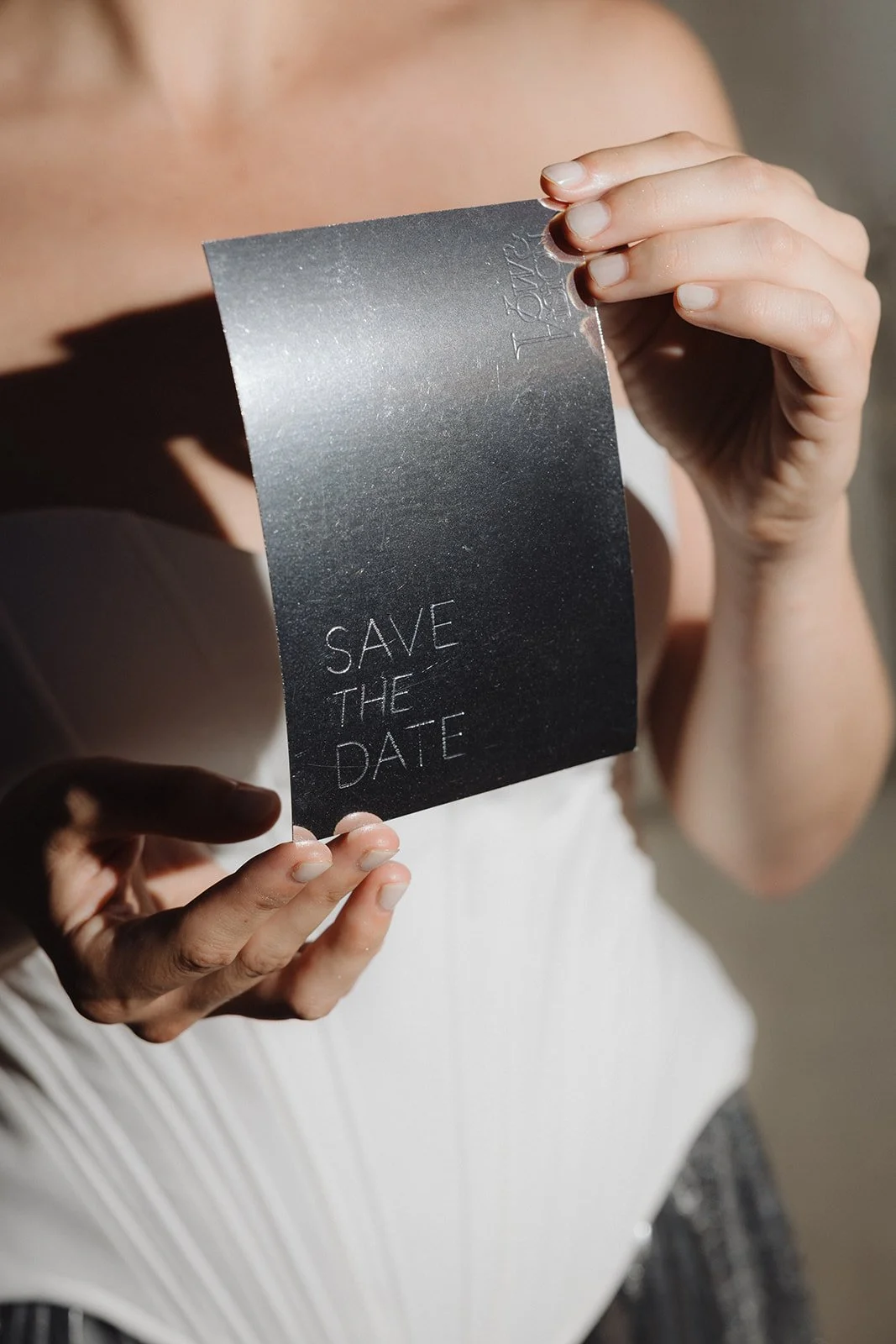 Close-up of a woman holding a black save the date card with metallic finish that reads 'SAVE THE DATE' in white text.