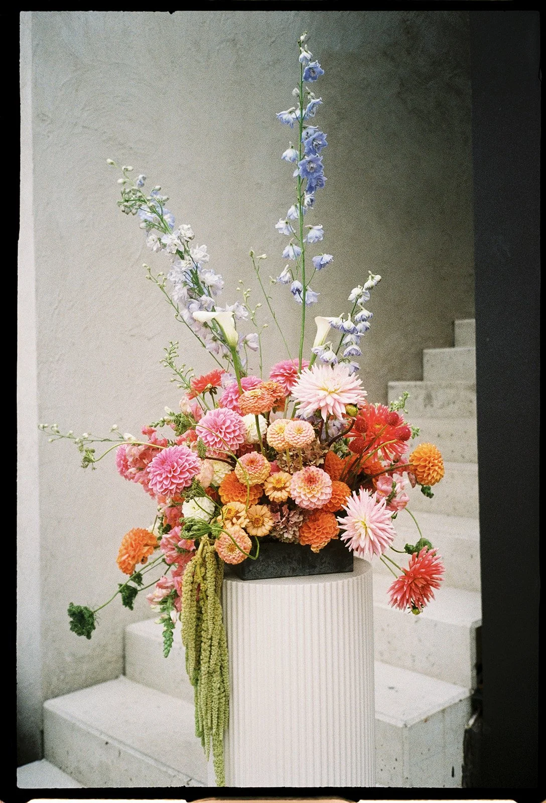 A colorful flower arrangement with pink, orange, and purple flowers on a white pedestal near stairs.