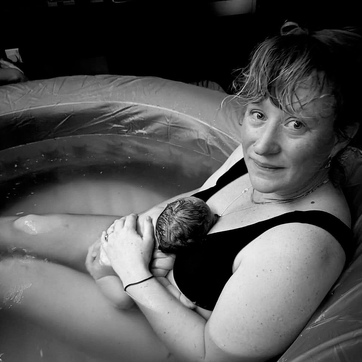 A woman who has just given birth at home, holding a new-born baby and sitting in a birthing pool.