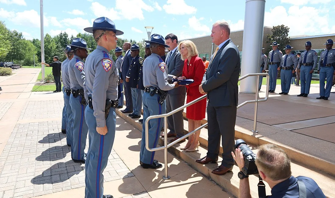Police officers receive awards from officials during a formal outdoor ceremony, with some officers lined up in uniform and others paying attention.