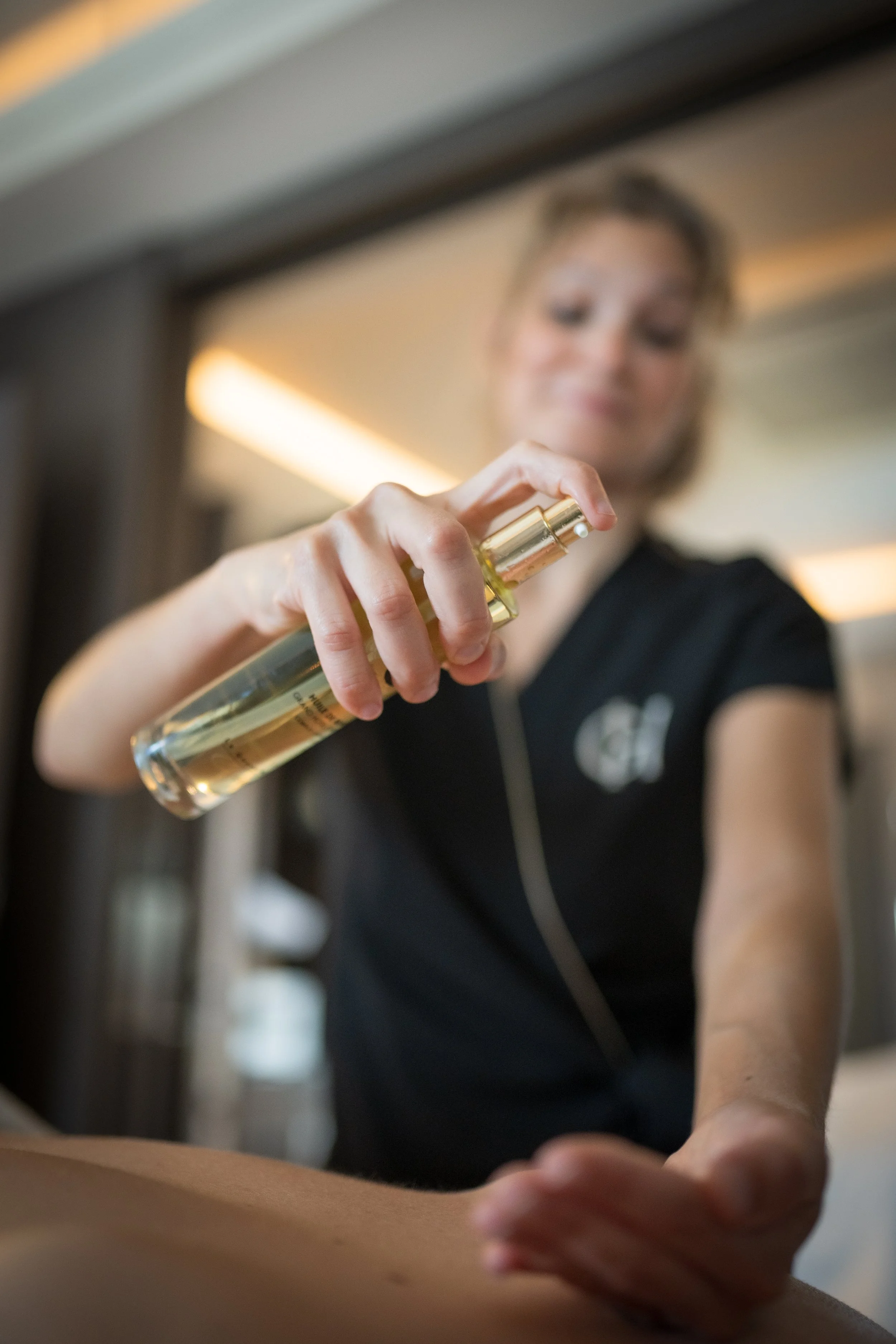 Une femme souriante tient une bouteille de parfum en spray, flou en arrière-plan.
