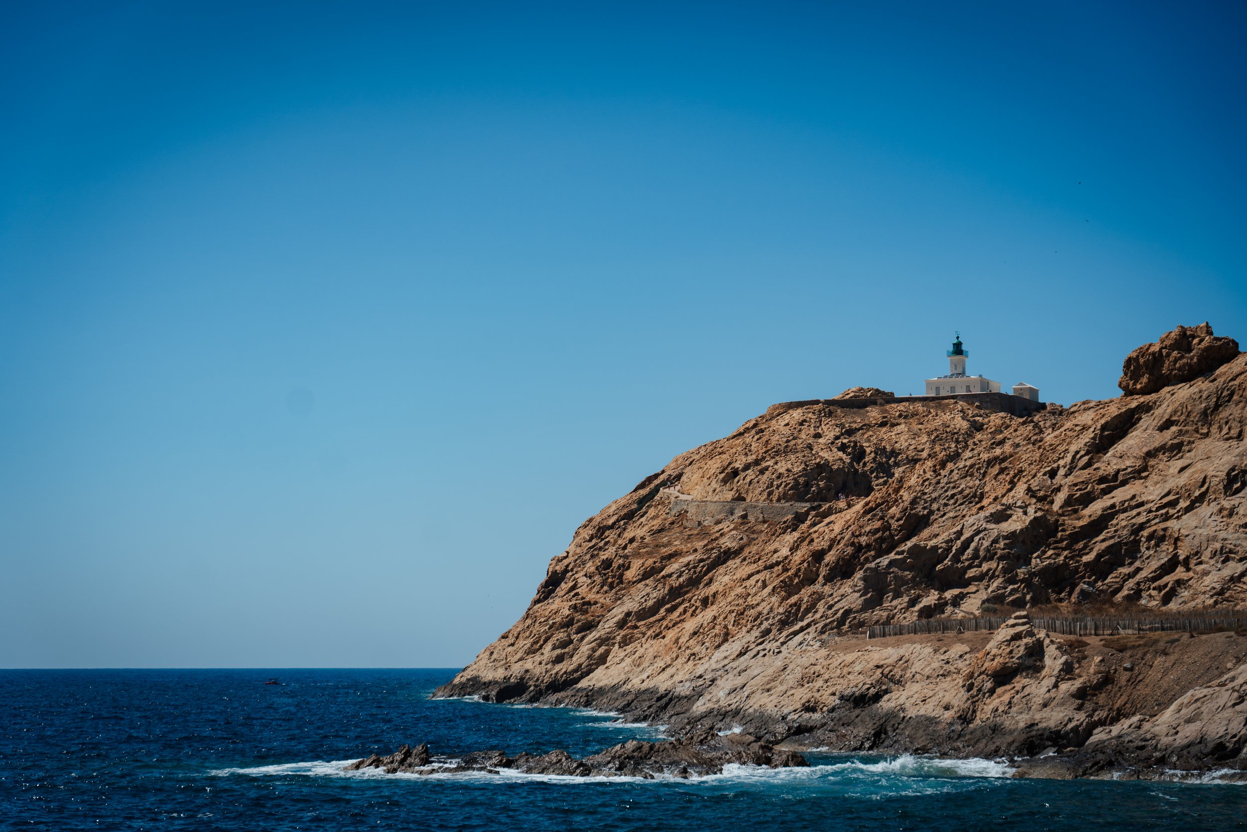 Phare sur une falaise rocheuse au bord de l'océan, ciel bleu clair.