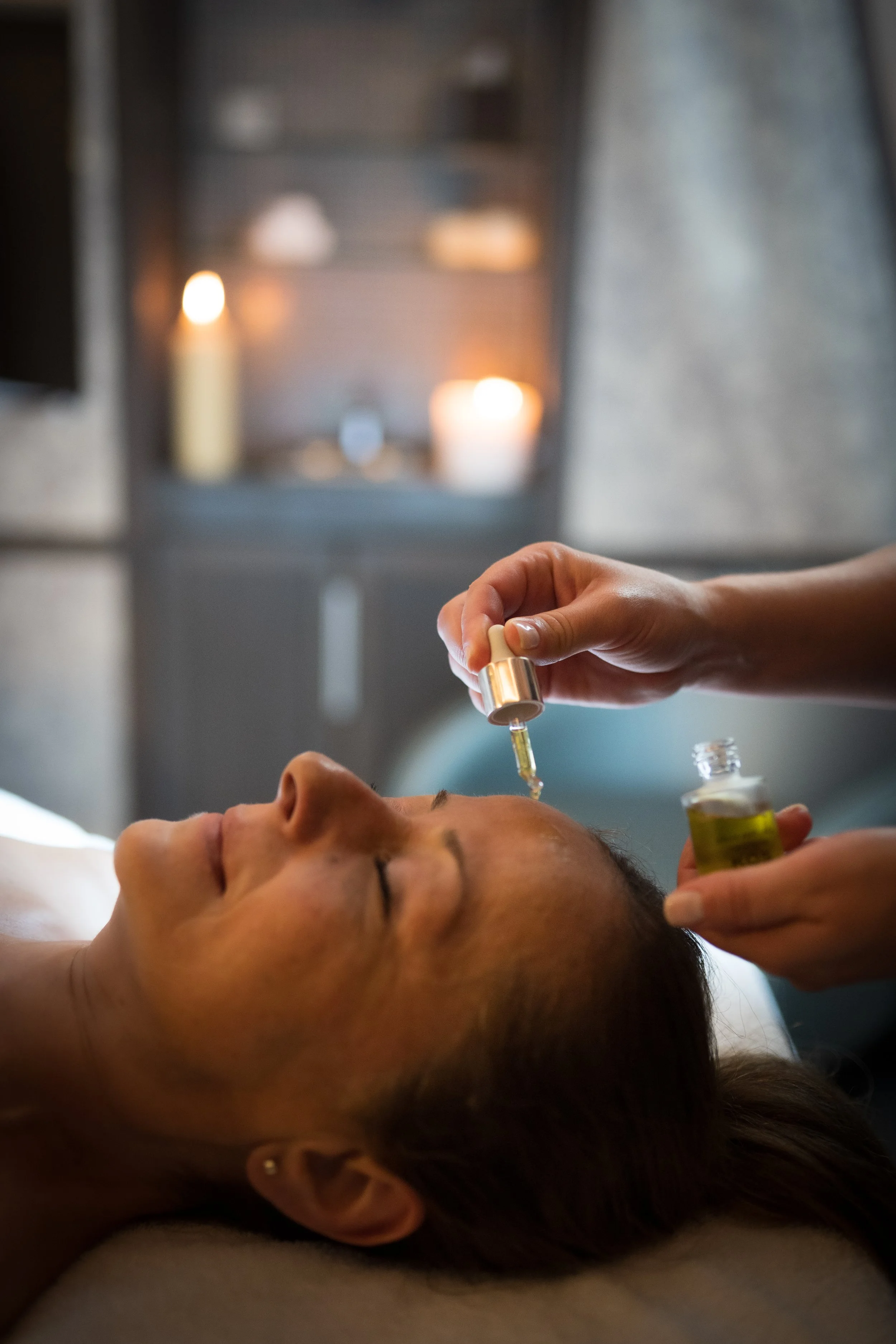Une personne reçoit une séance d'acupuncture ou d'injection sous la joue, allongée sur une table, dans un cadre calme et relaxant avec des bougies en arrière-plan.