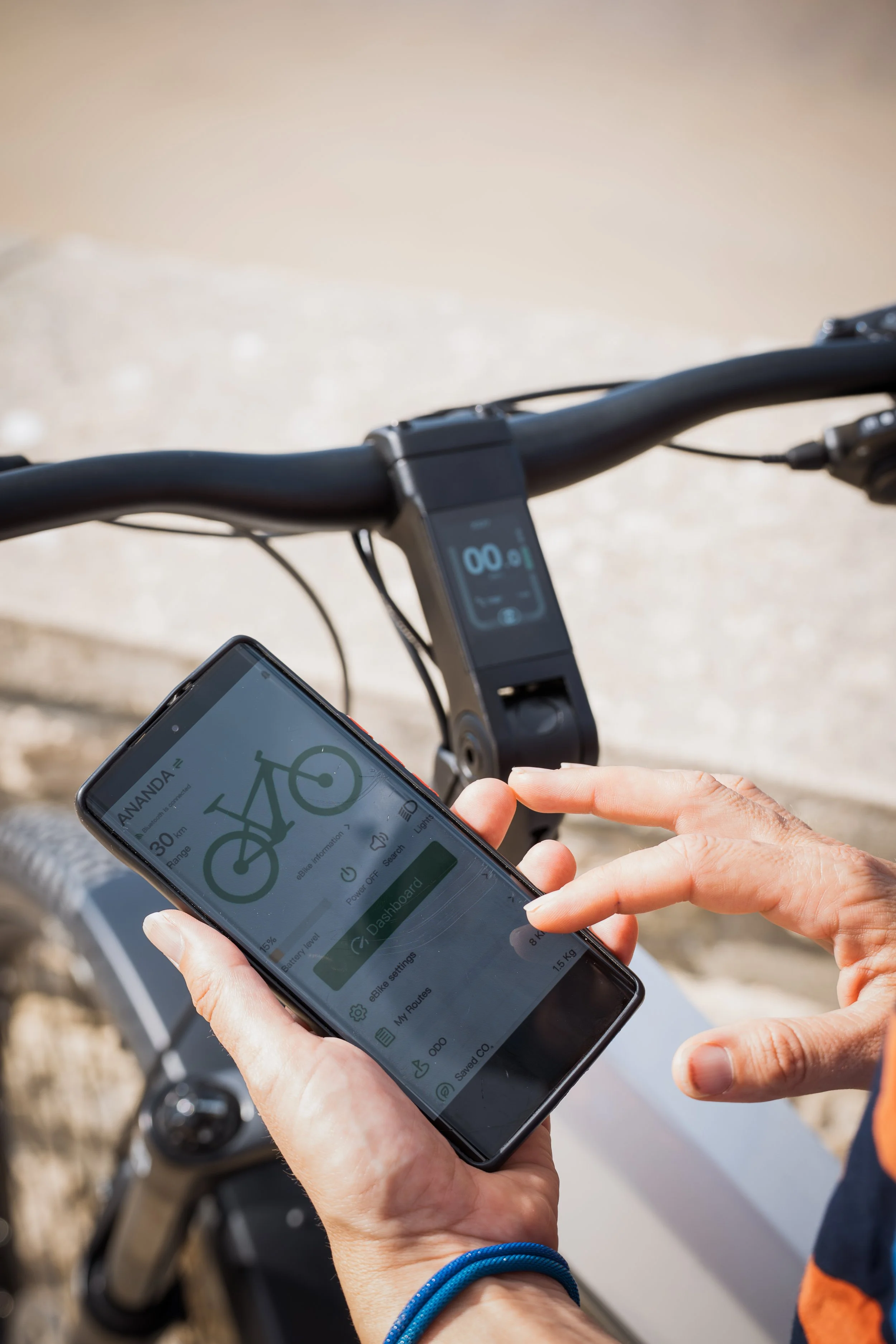 Personne utilisant une application de vélo sur un smartphone, avec un vélo électrique en arrière-plan, pour vérifier ou régler le mode de fonctionnement.