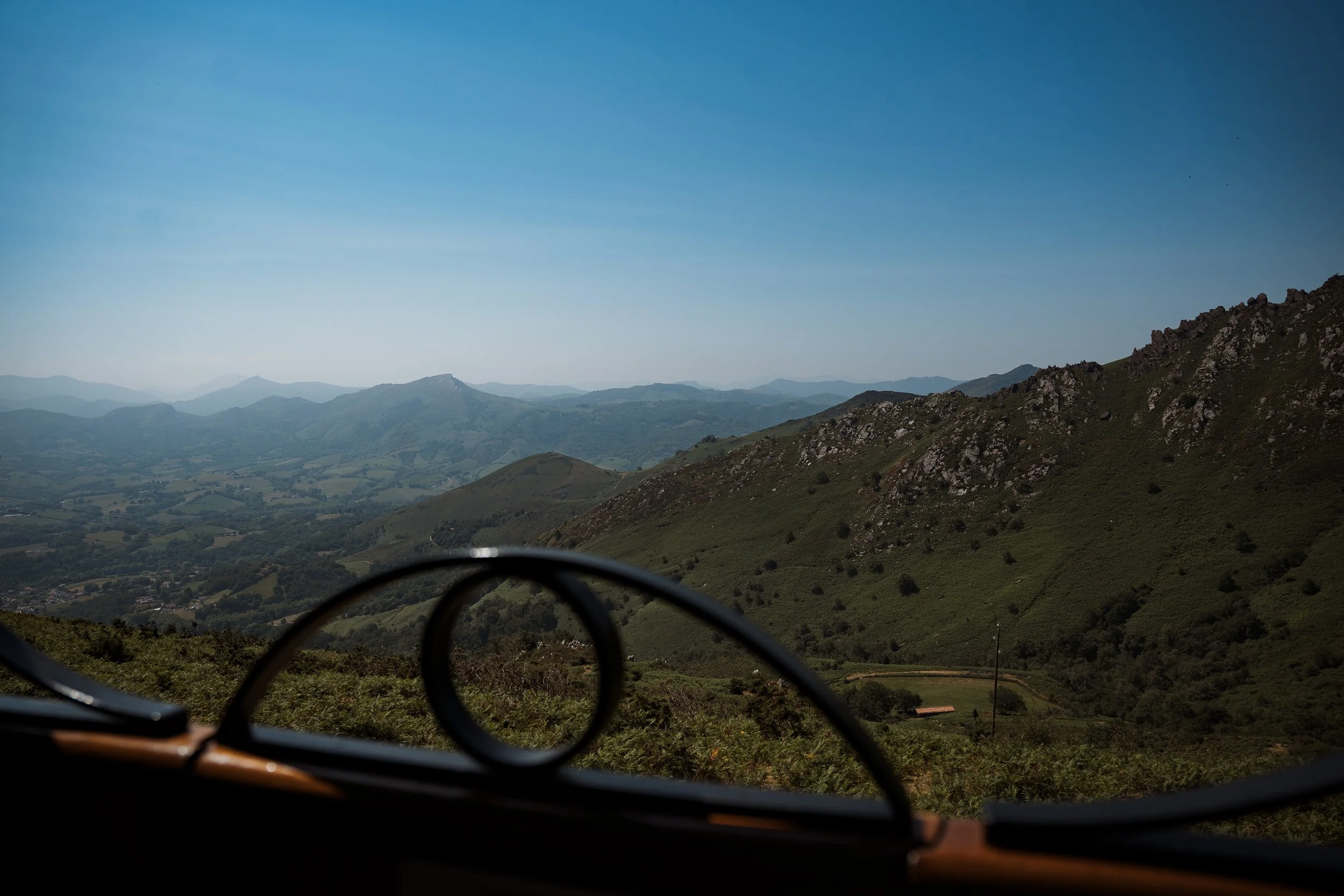 Paysage de montagnes avec des collines verdoyantes et un ciel bleu clair, vu depuis l'intérieur d'une voiture.