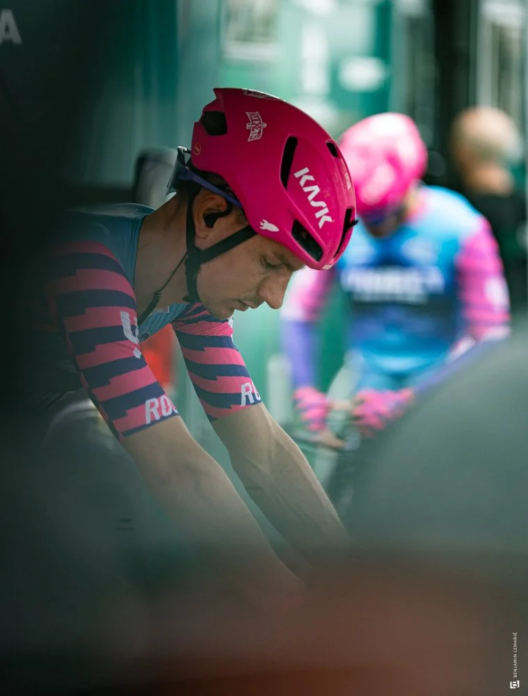 Un cycliste portant un casque rose et un maillot à rayures roses et noires, préparé pour une course ou une séance d'entraînement.