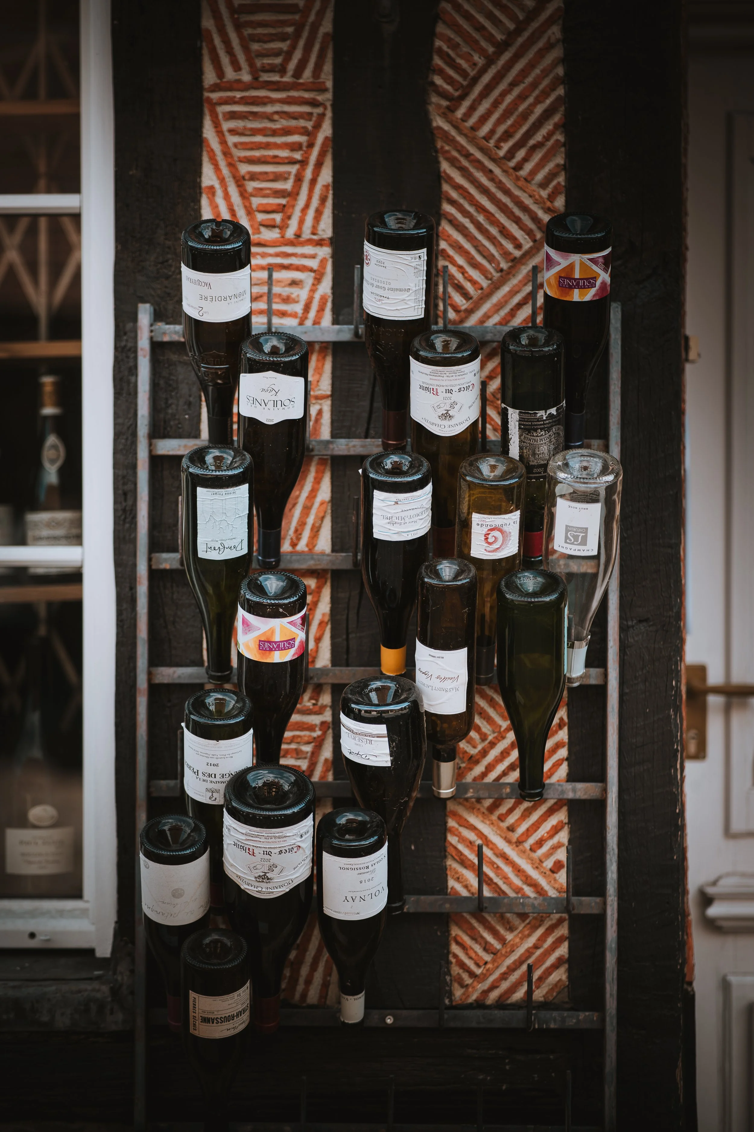 Vitrine à vin avec plusieurs bouteilles de vin rangées à l'envers sur une structure en métal, fond en brique rouge et noire.