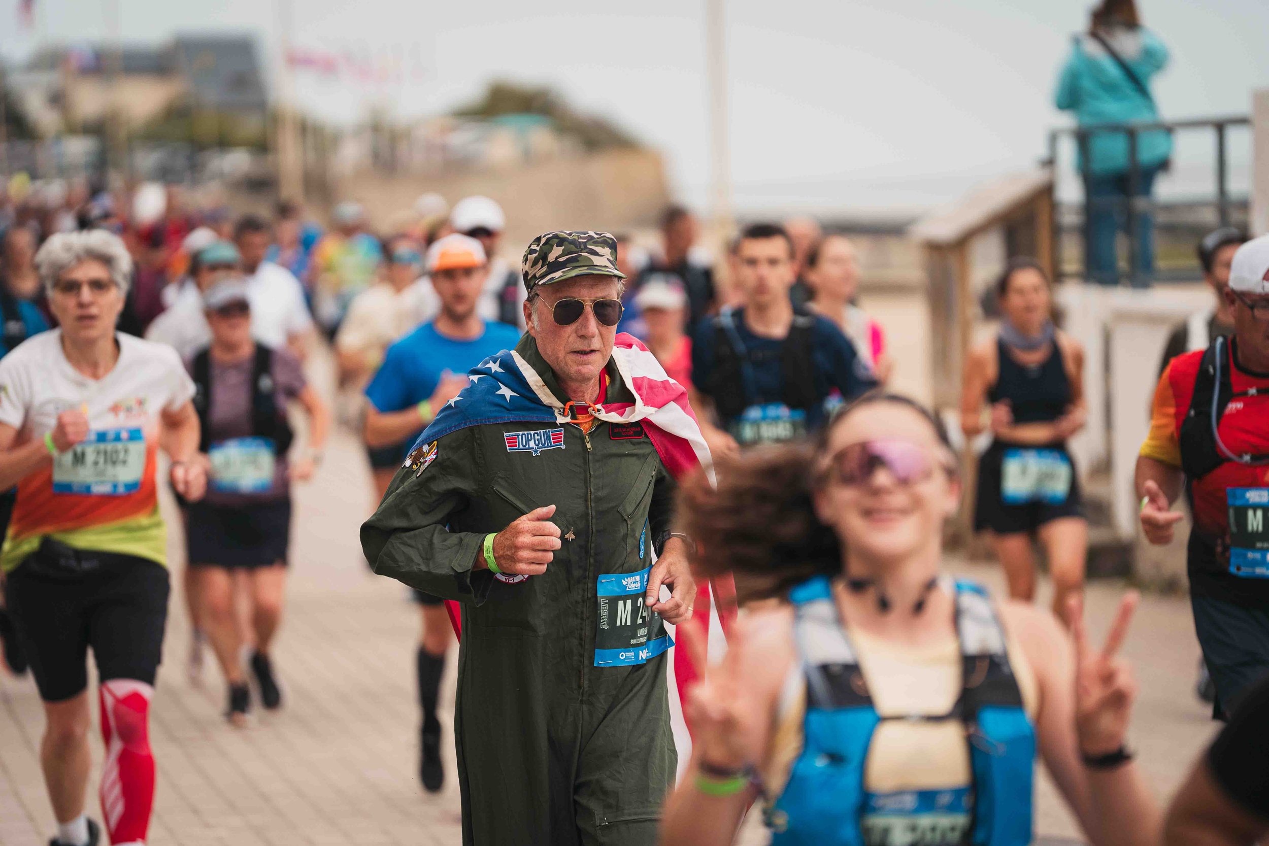 Groupe de coureurs participant à une course organisée, parmi eux un homme portant un drapeau américain, des numéros de course et des vêtements de sport.