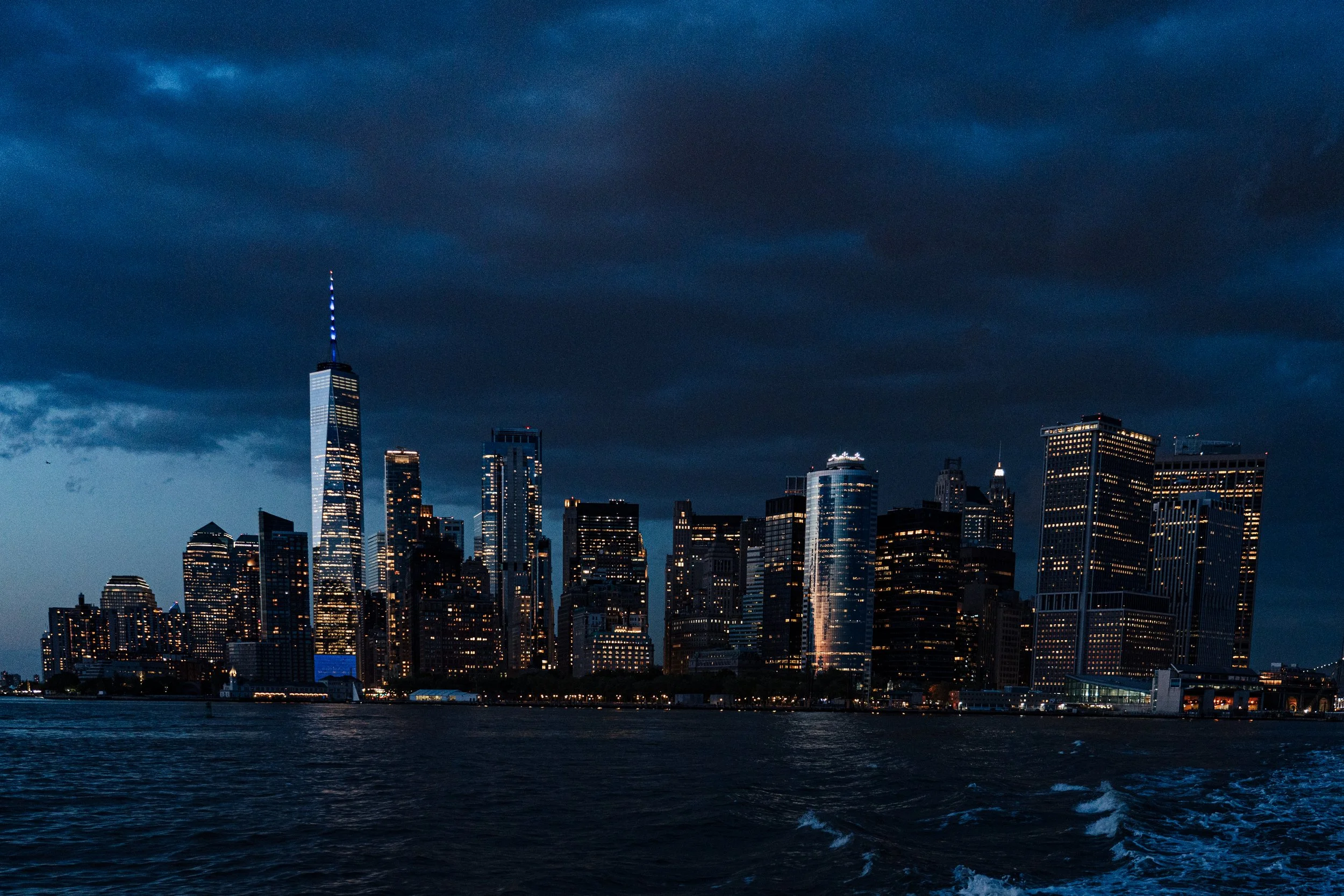 Vue de la skyline de New York la nuit, avec des immeubles illuminés et un ciel nuageux au-dessus de l'Hudson River.