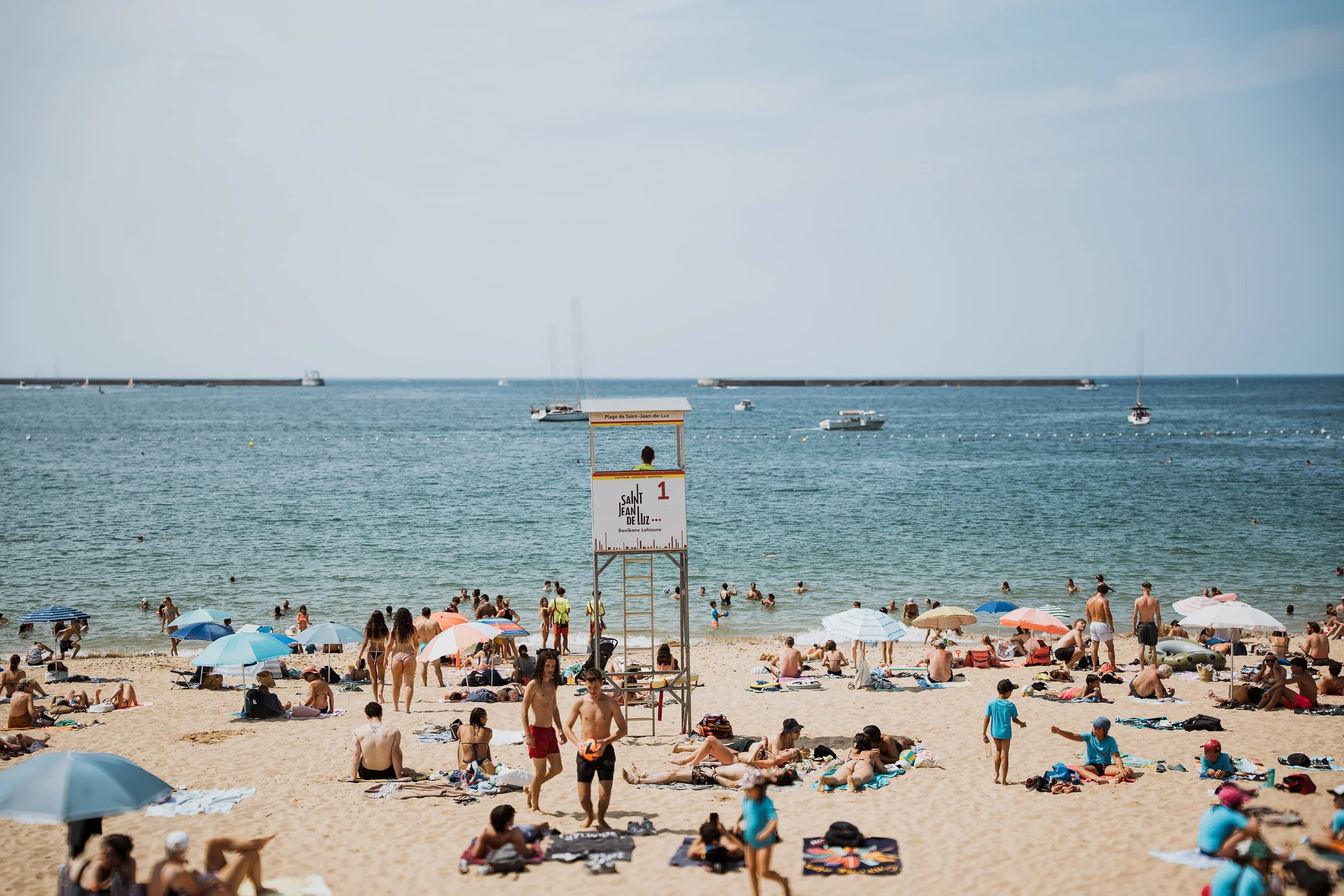 Plage de Saint-Jean-de-Luz avec des touristes, parasols colorés, vie quotidienne en bord de mer.