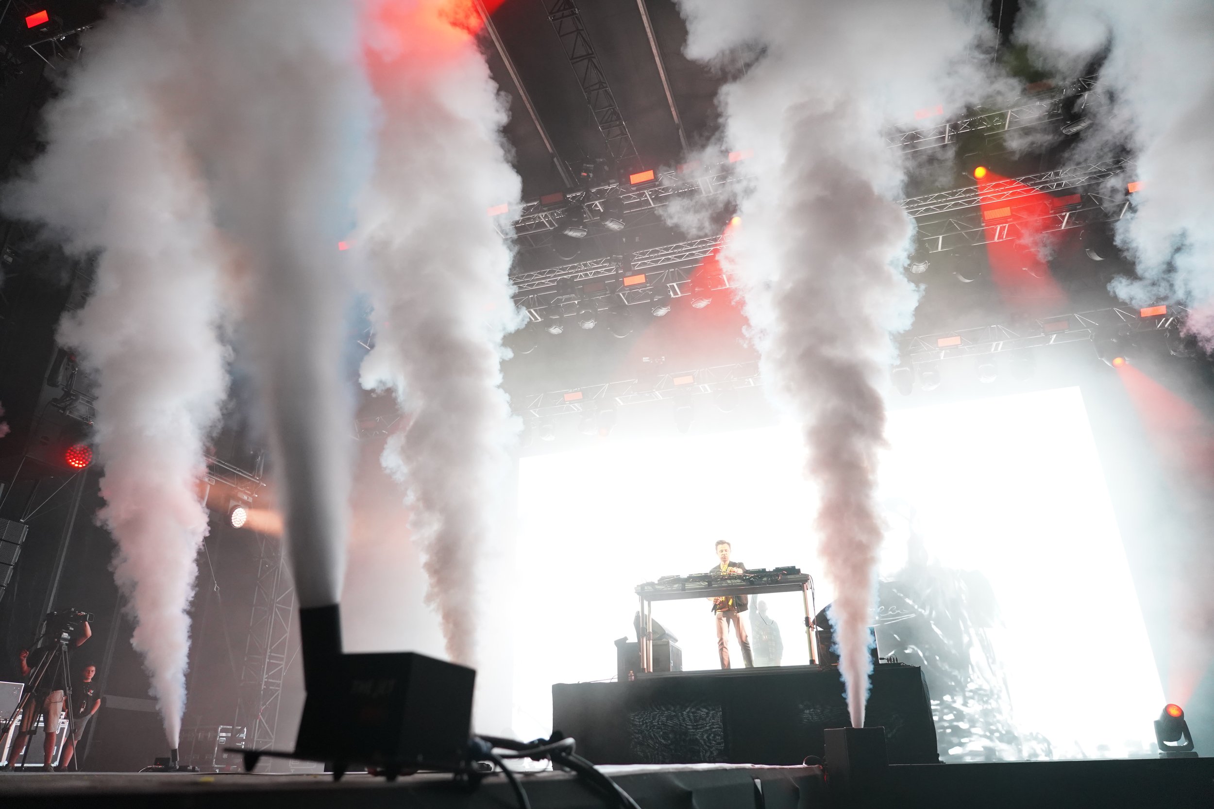 Un DJ se produit sur scène avec des fumées et des effets lumineux lors d'un concert.