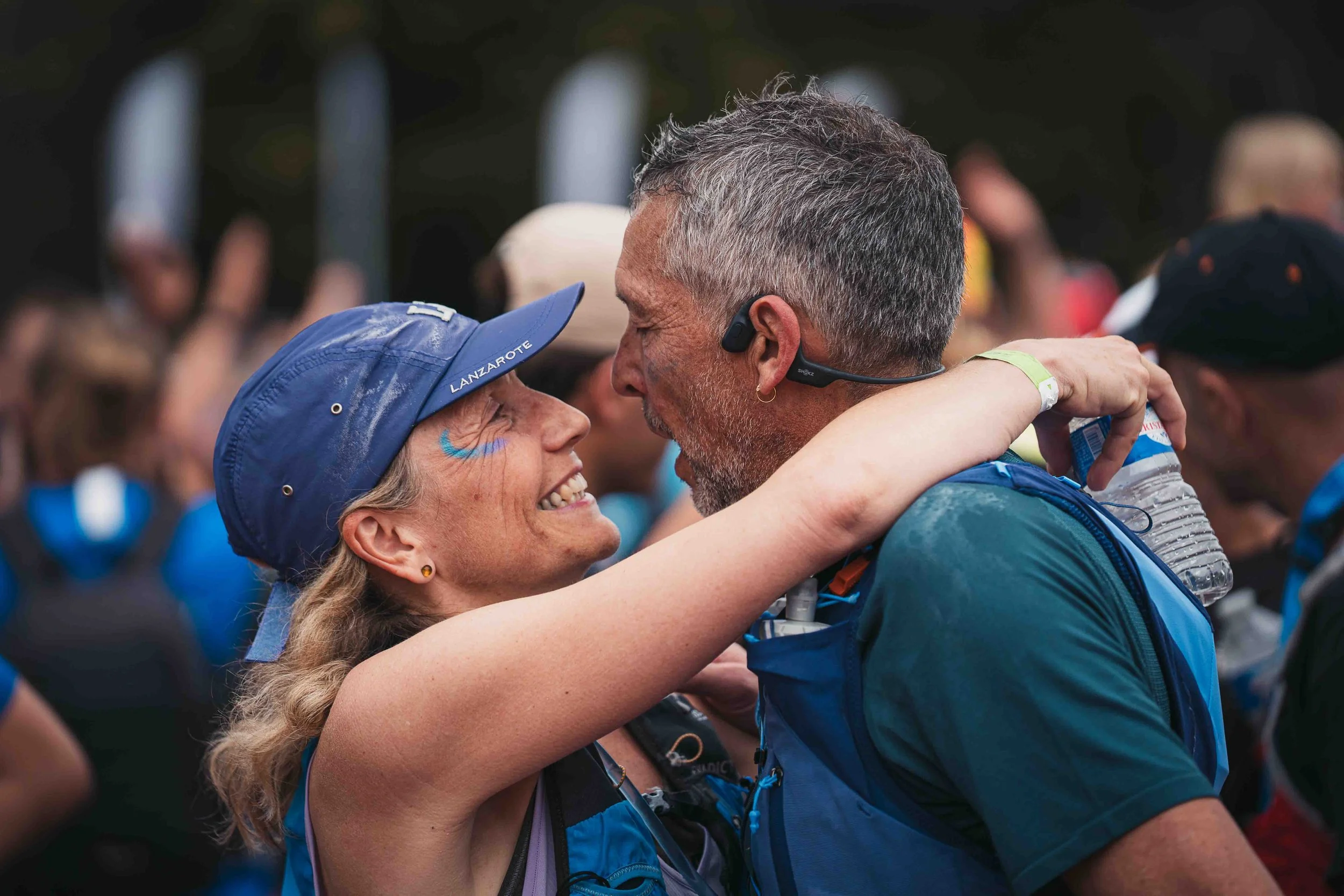 Une femme et un homme s'étreignent lors d'une course ou d'un événement sportif, souriants, entourés d'autres participants.