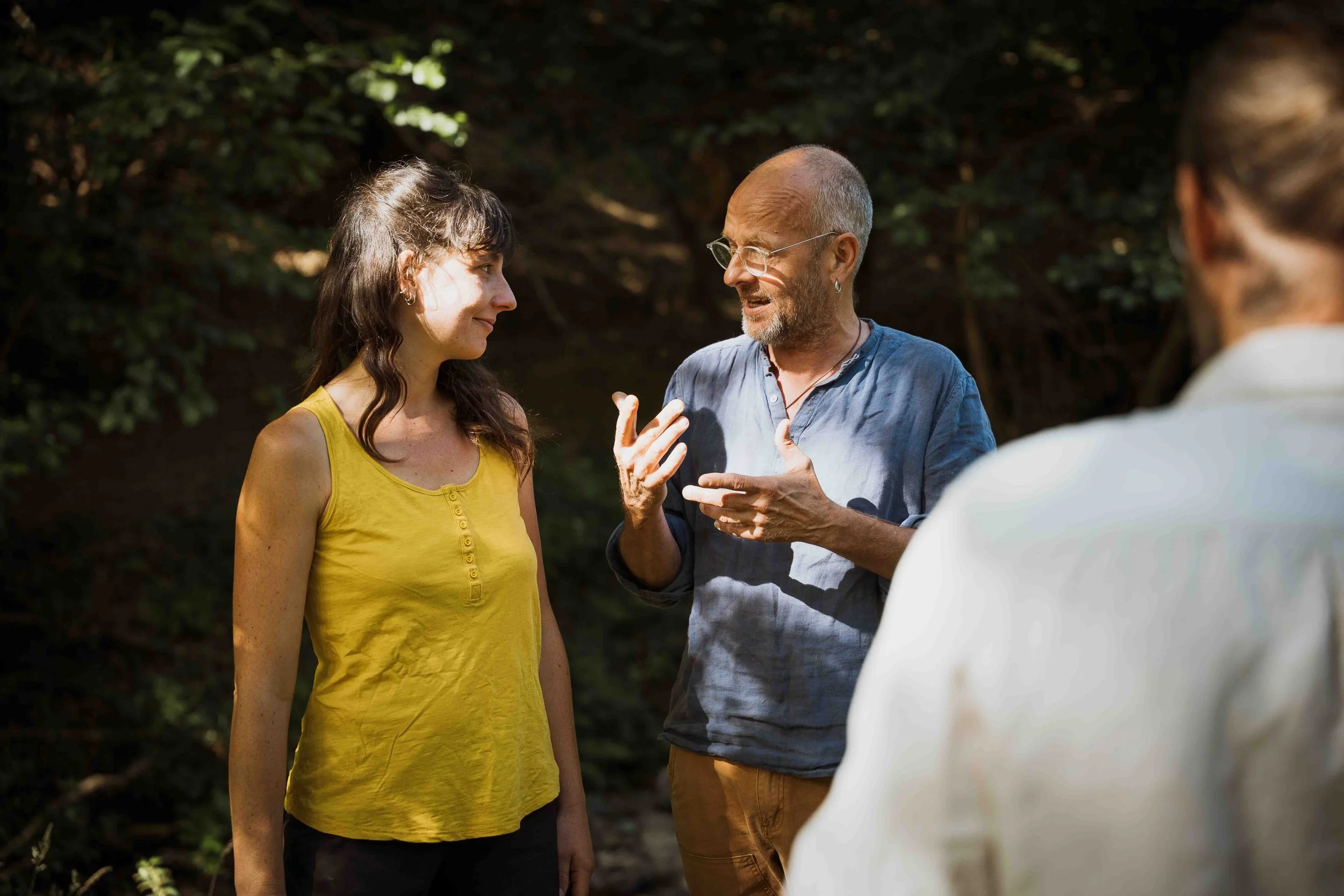 Un groupe de trois personnes en conversation en plein air, avec un arrière-plan de végétation, en train de discuter.