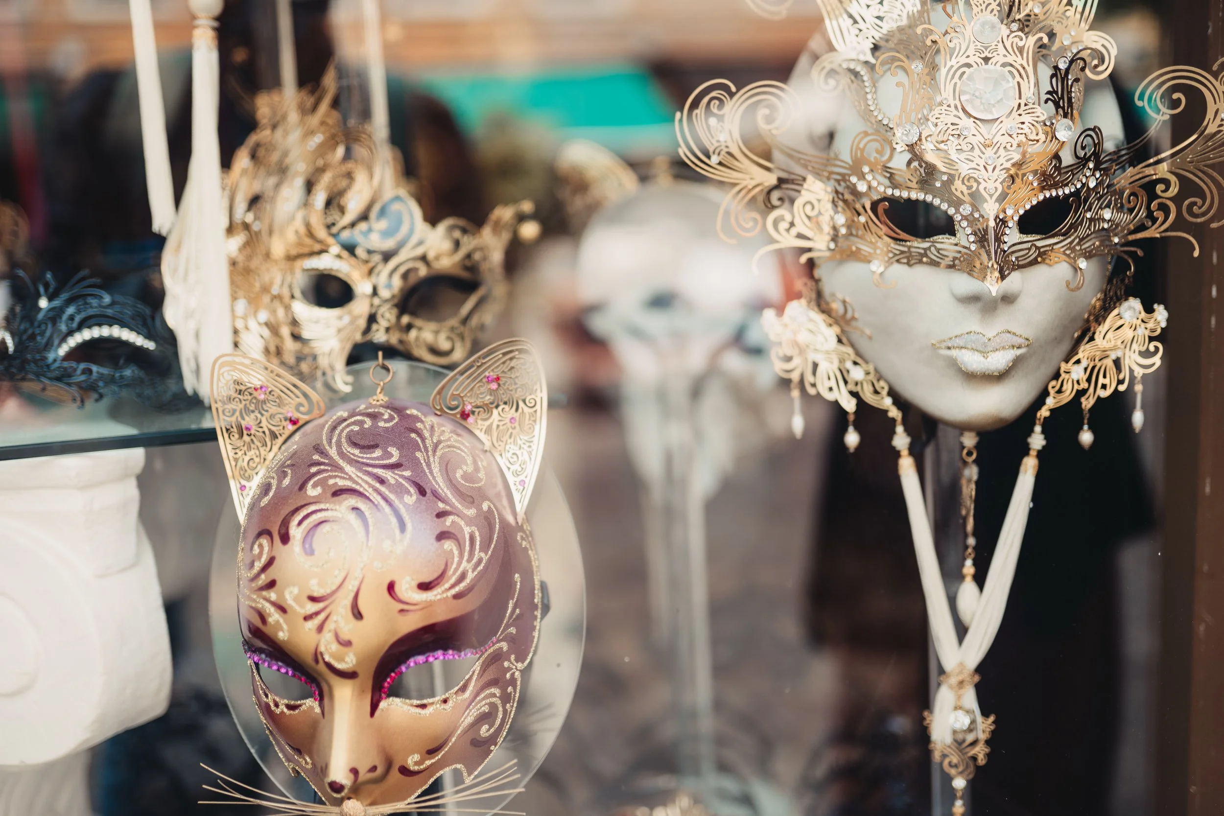 Masques de carnaval décorés avec des détails dorés et des bijoux, exposés en vitrine.