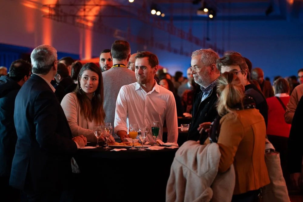 Groupe de personnes discutant lors d'une soirée ou d'un événement formel, avec des boissons sur la table.