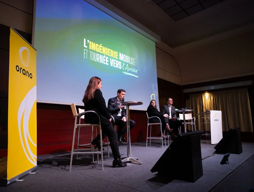 Une conférence ou un panel avec quatre intervenants assis sur scène, un écran derrière eux affiche le titre 'L'ingénierie mobilisée et tournée vers l'avenir', et une bannière à gauche avec le logo 'orano'.