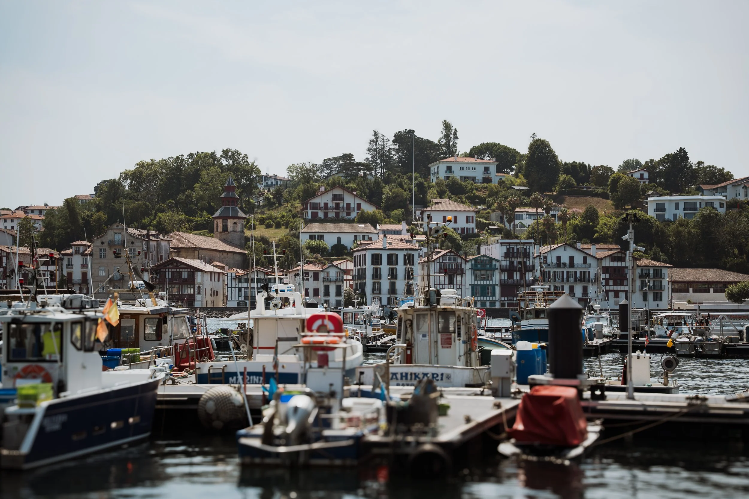 Port de bateaux avec maisons en arrière-plan, situées sur une colline. Le ciel est dégagé.