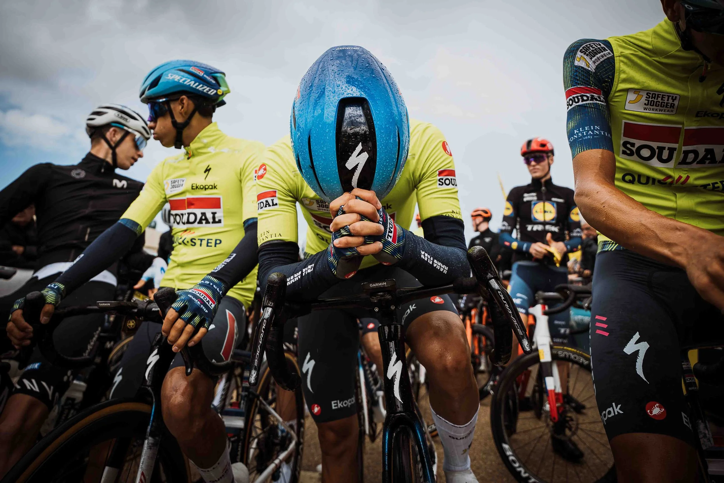 Cyclistes en tenue de compétition, certains portant des casques, alignés sur des vélos de course lors d'une course ou d'une épreuve.