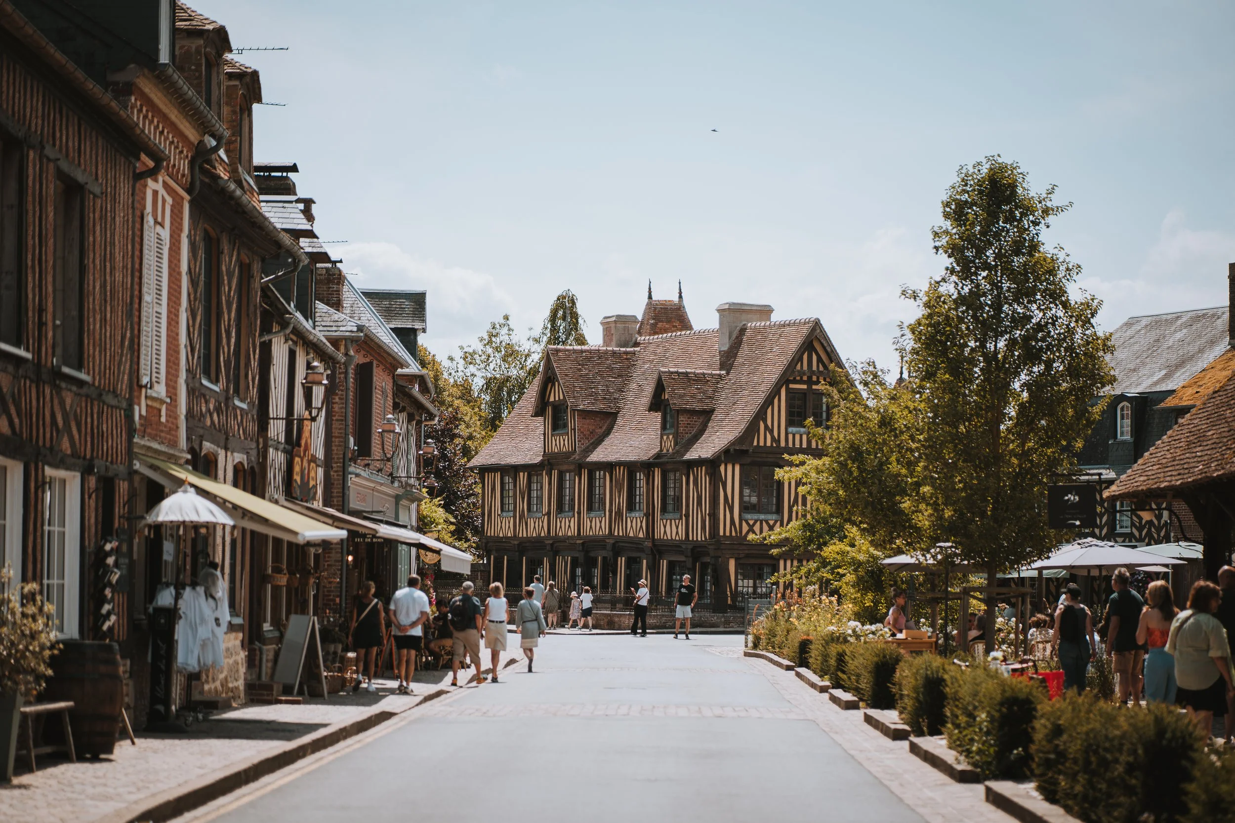 Une rue piétonne avec des bâtiments à architecture traditionnelle, des gens se promenant et des terrasses de cafés sous un ciel ensoleillé.