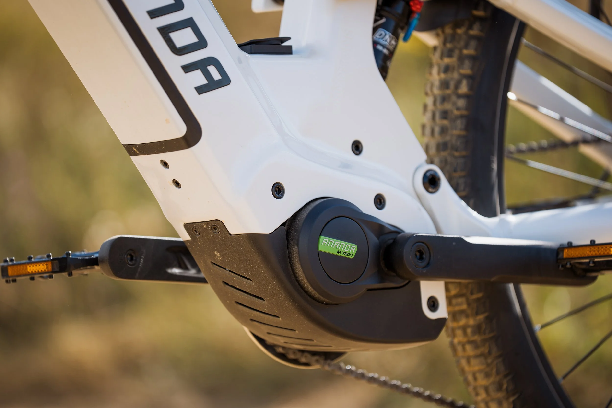 Une image en angle rapproché d'une partie d'une moto électrique. La pièce visible est une zone blanche avec des vis noires, et un cercle noir portant le label vert 'ANANO M7200'.