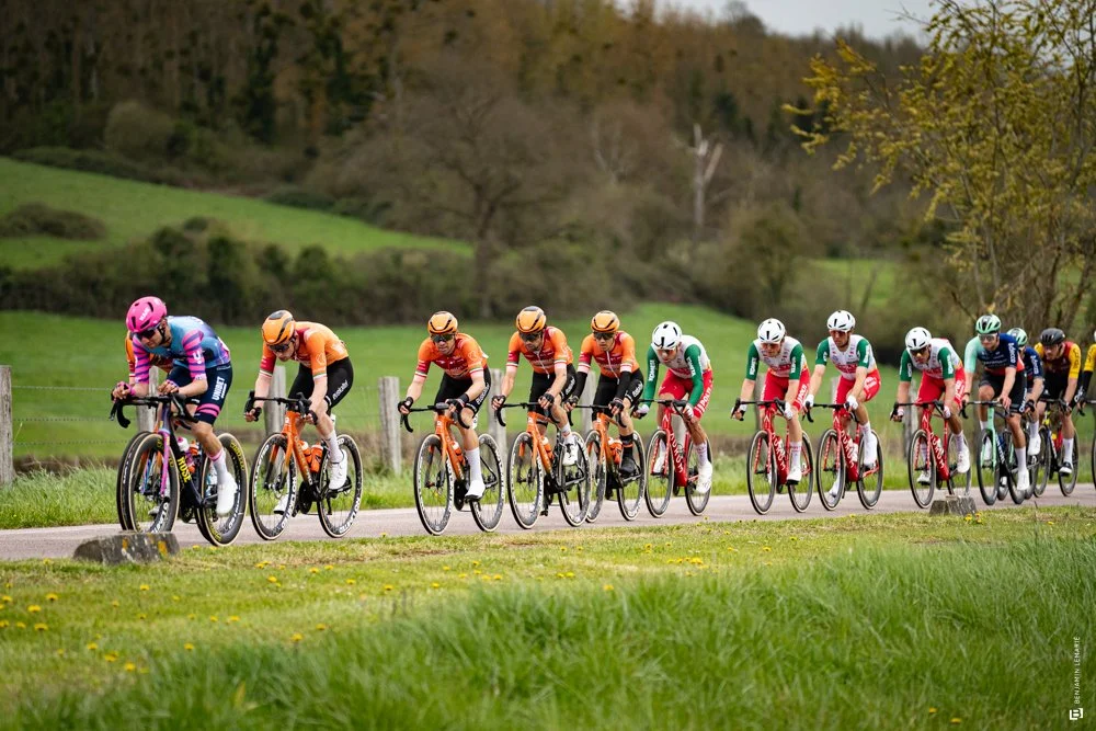 Groupe de cyclistes en compétition sur une route rurale avec un paysage verdoyant en arrière-plan.