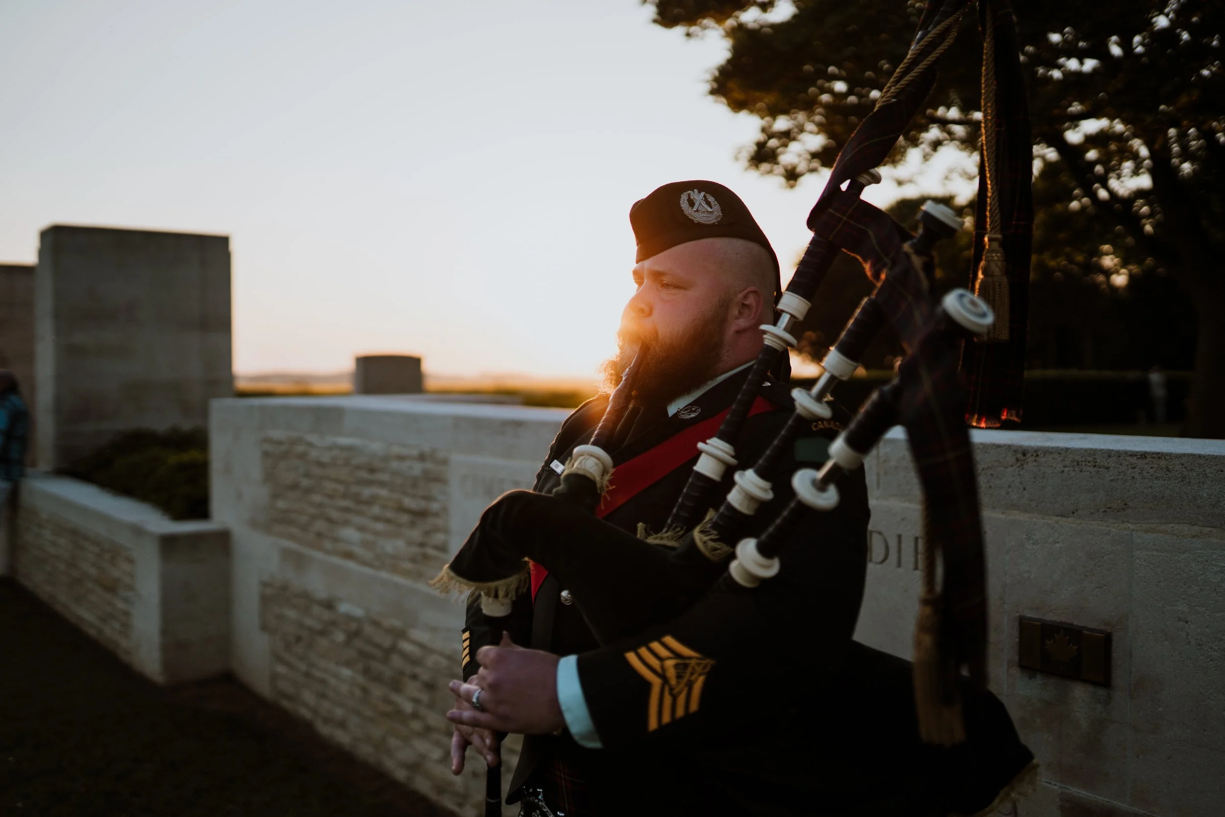 Un homme en uniforme de militaire jouant de la cornemuse lors d'un coucher de soleil