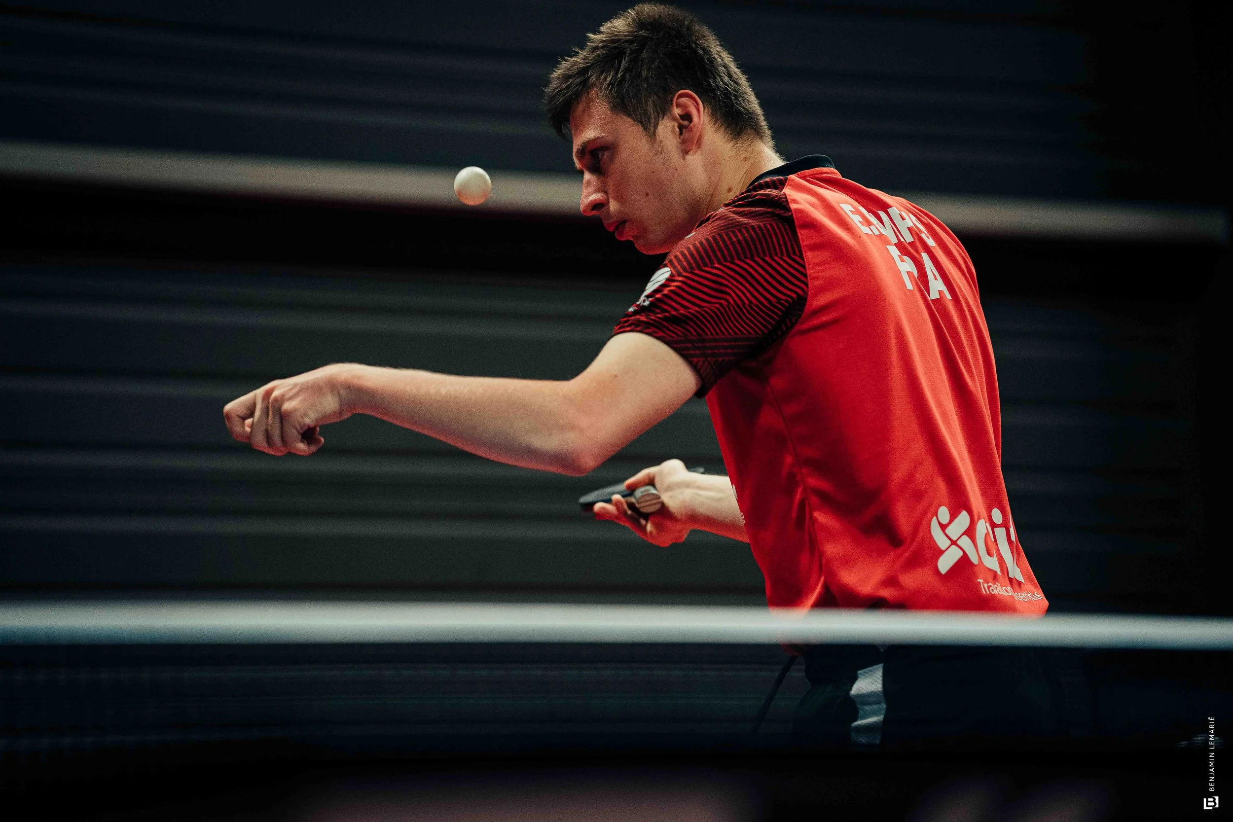 Jeune homme jouant au tennis de table, concentré, en direction d'une balle qui vole.