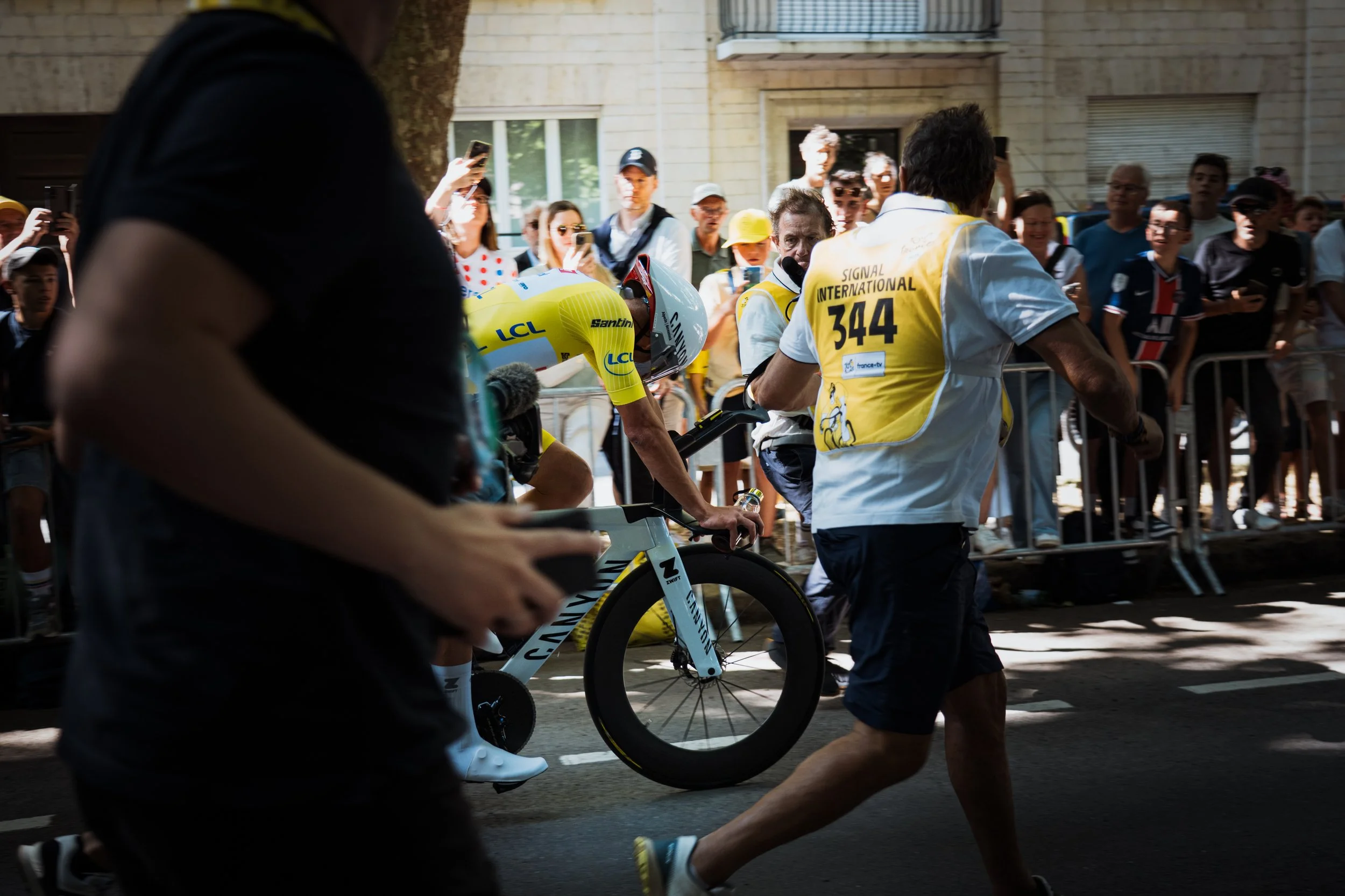 Un cycliste en maillot jaune traversant la ligne d'arrivée lors d'une course, entouré de spectateurs qui prennent des photos et encouragent.