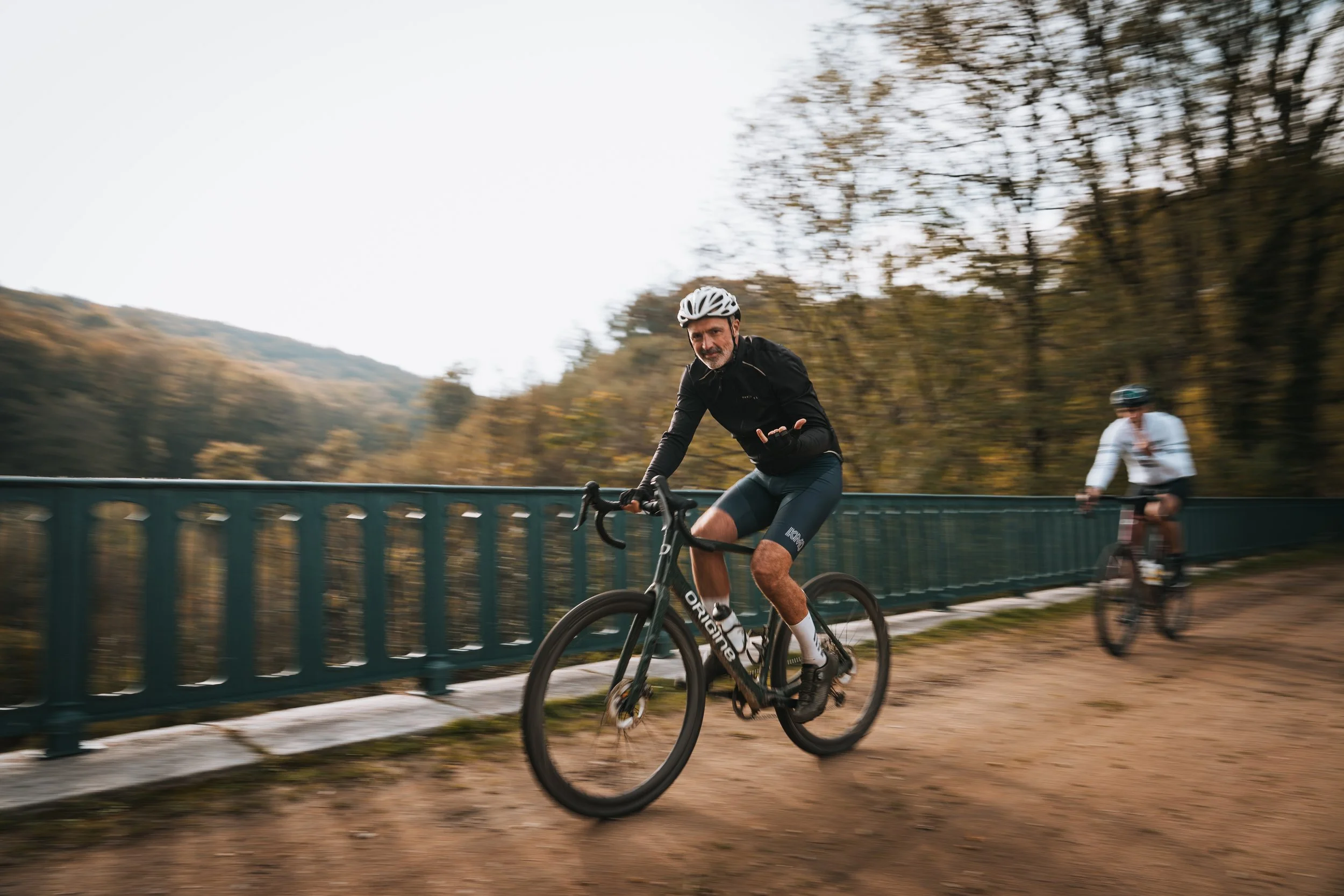 Un homme faisant du vélo sur un pont entouré d'arbres, avec un ciel clair en arrière-plan.