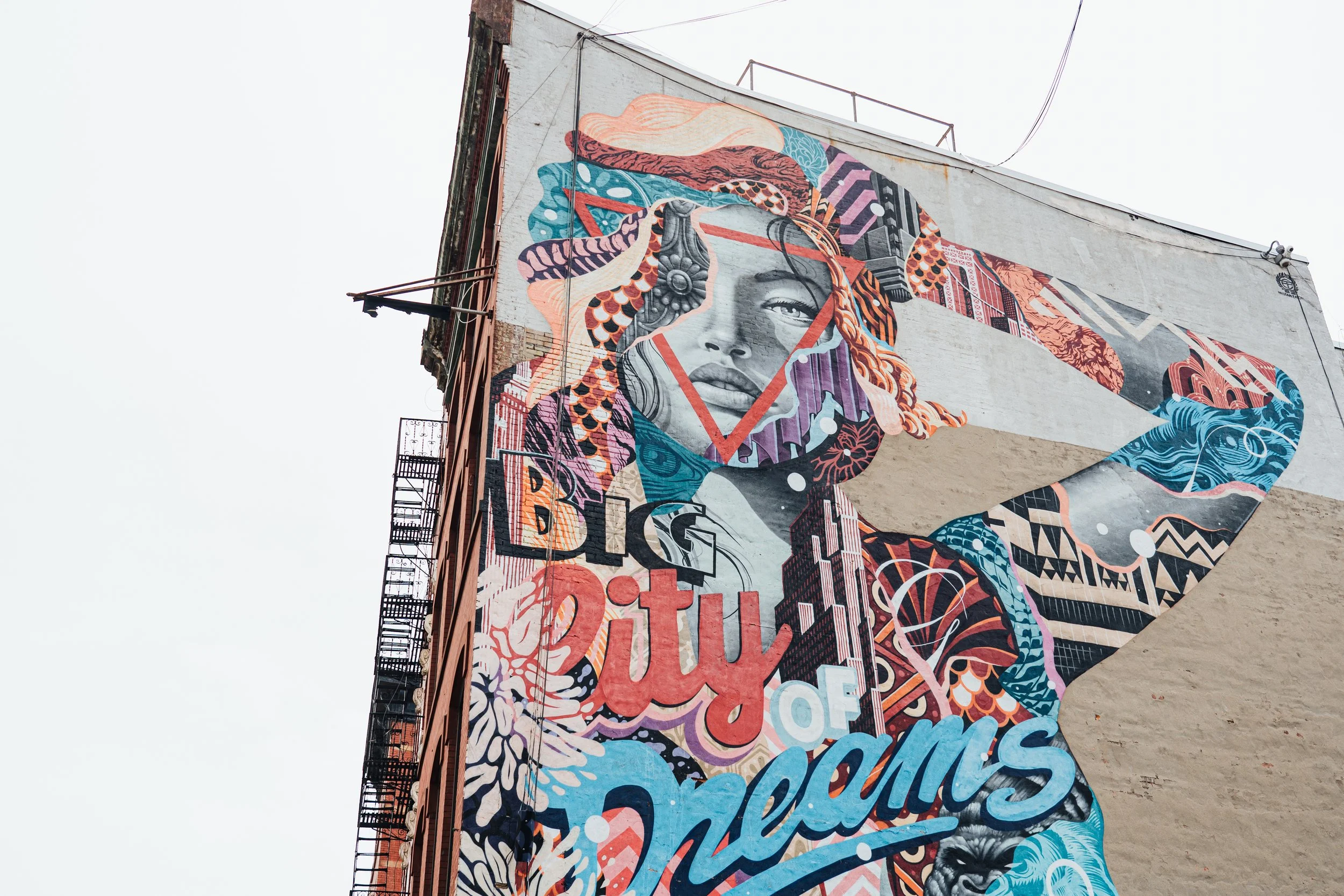 Graffiti mural représentant un visage d'une femme avec des cheveux colorés et des éléments graphiques, sur un bâtiment.