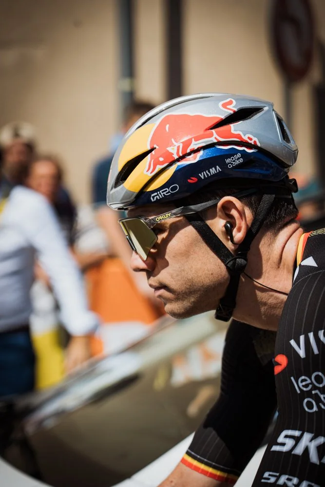 Cycliste professionnel portant un casque Red Bull, lunettes de soleil, et maillot de course, en préparation pour une compétition.