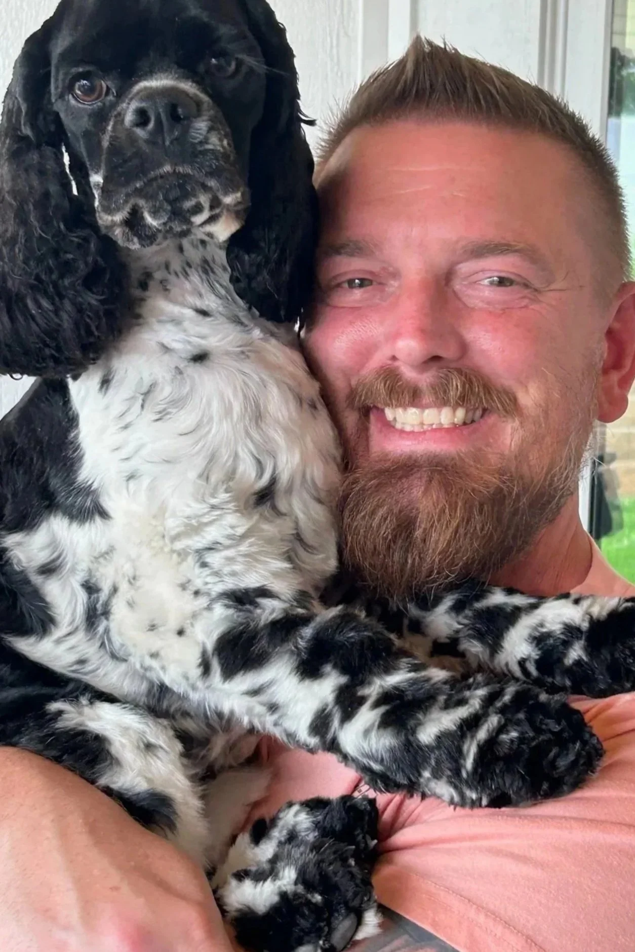 A man with a beard smiling while holding a black and white English Springer Spaniel puppy close to his face.