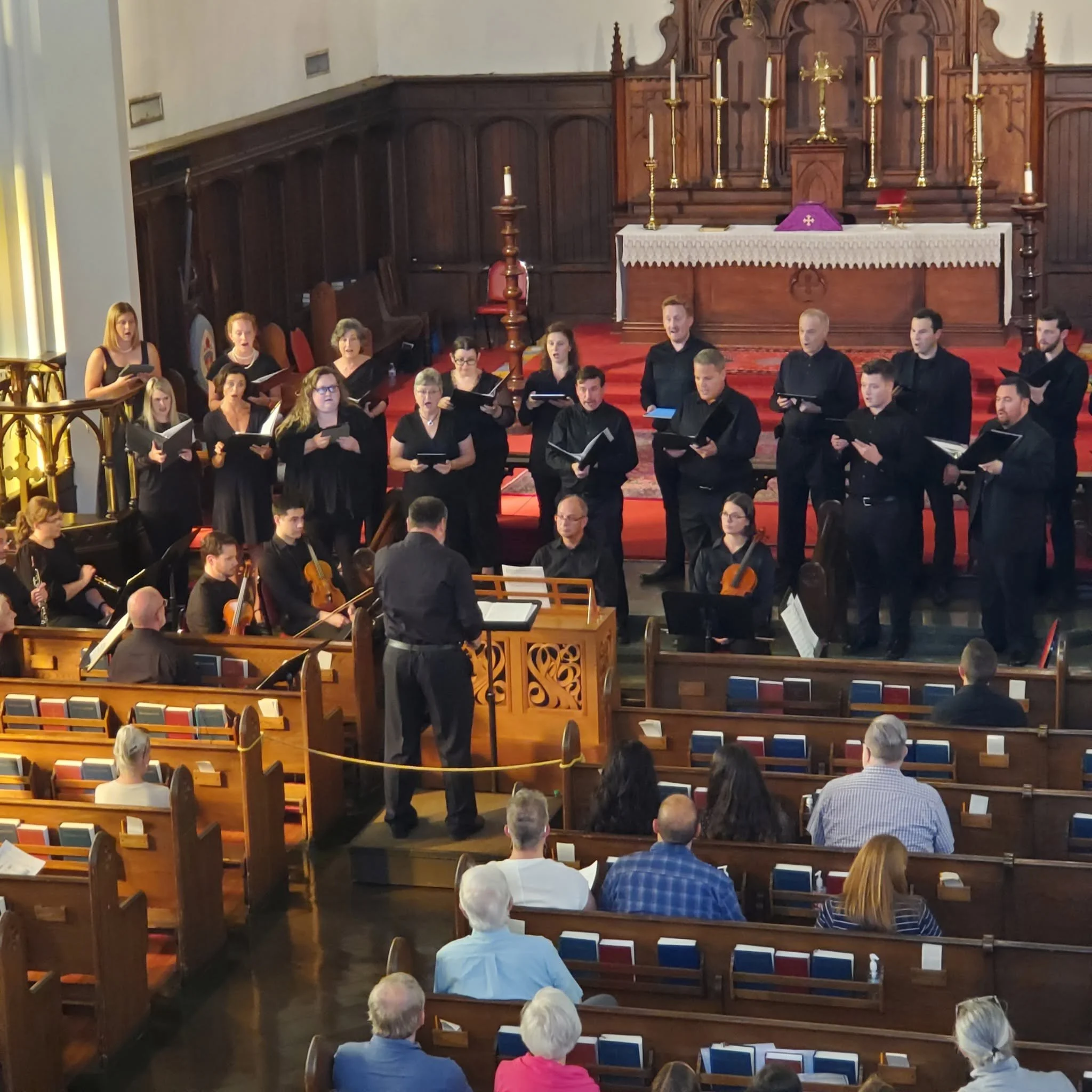 Choir of men and women singing during church service inside a wooden church.