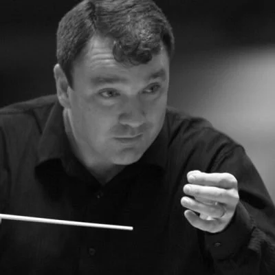 David Long conducting a choir and orchestra, holding a baton in his hand.