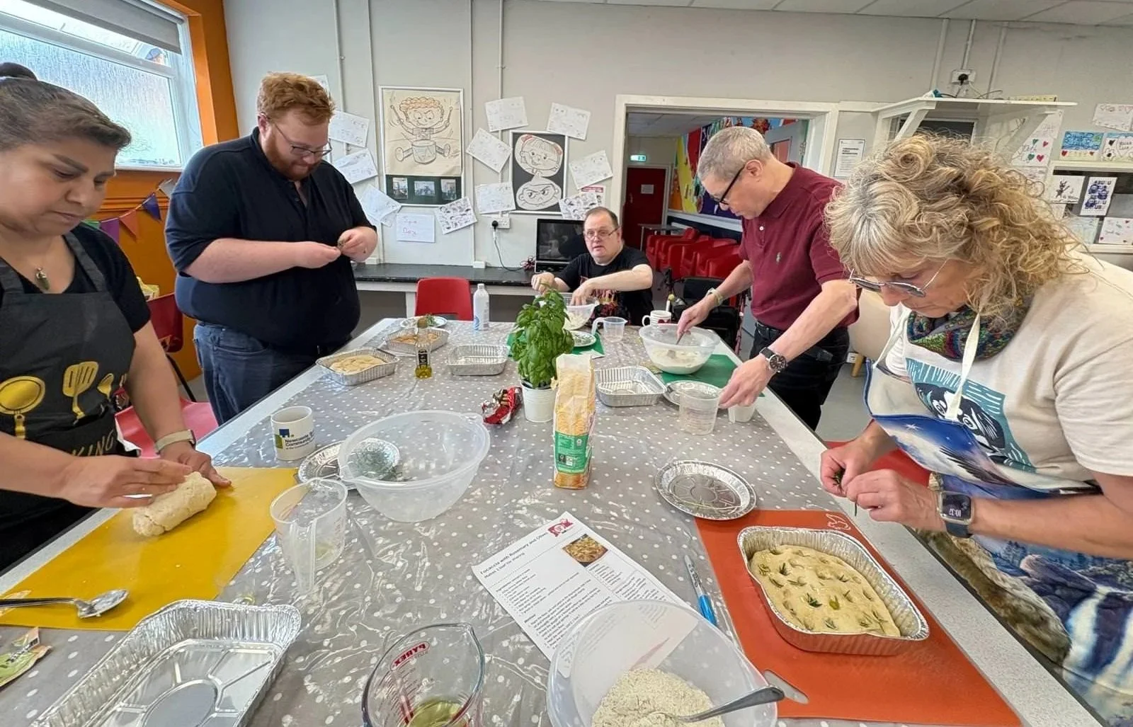 People preparing food in a community kitchen or cooking class, with ingredients and utensils on the table.