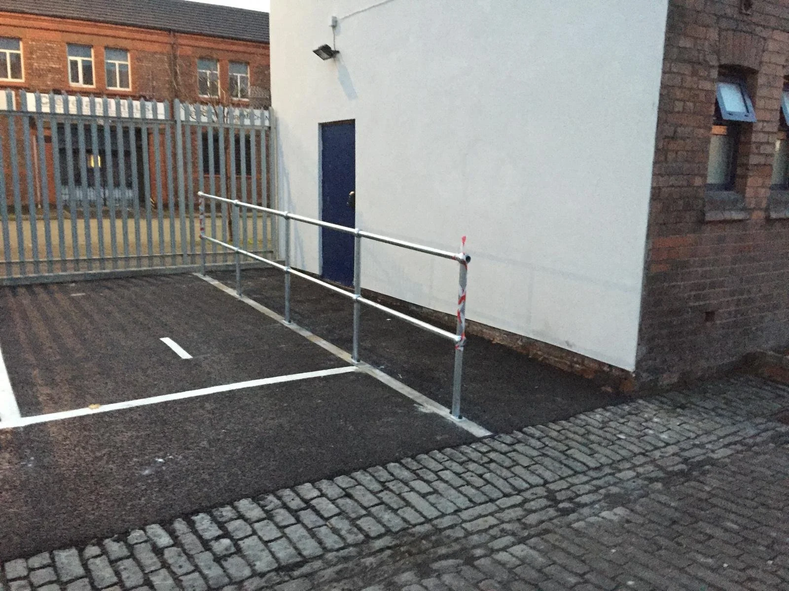 Empty parking space with safety barriers and a white building wall in an urban setting.