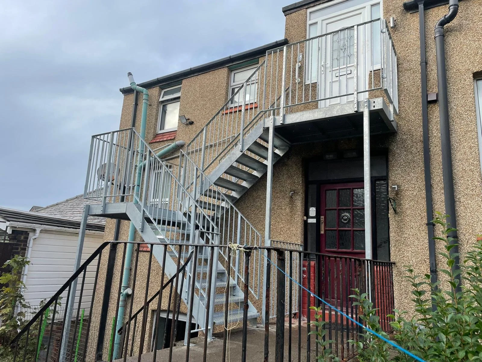 Exterior view of a multi-story building with an external metal staircase leading to the second-floor balcony and entrance door.