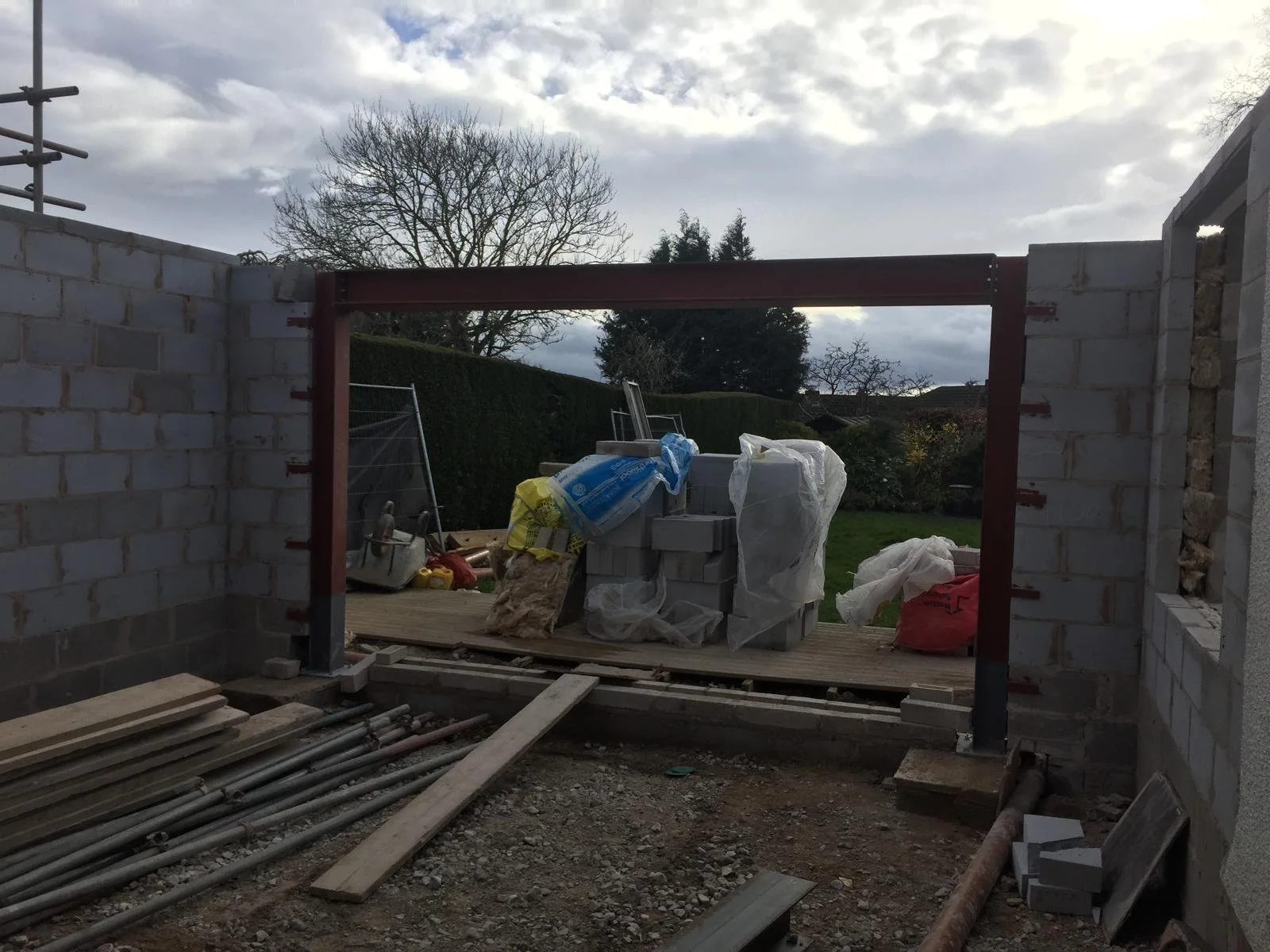 Construction site with brick walls, building materials, and tools. Overcast sky with trees in the background.