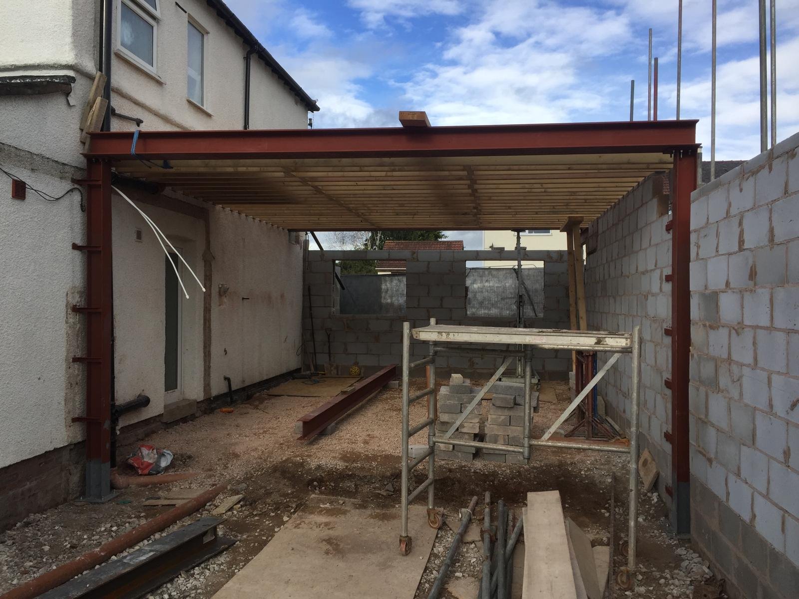 Construction site of a building with metal and brick framework, scaffolding, and unfinished walls.