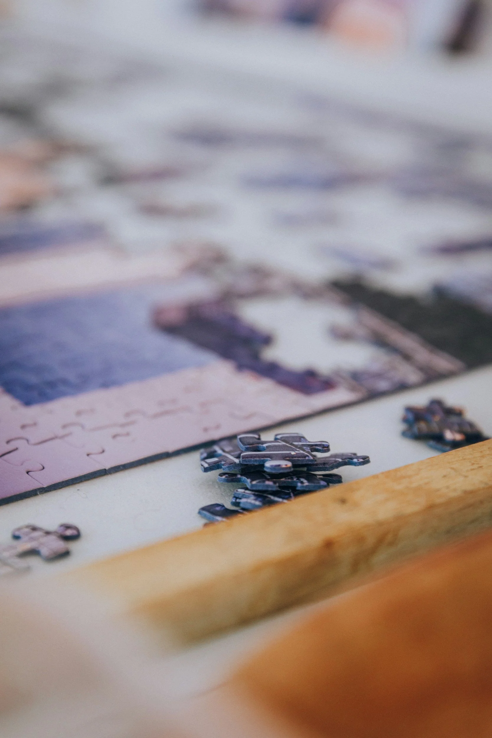 Close-up of scattered puzzle pieces on a white surface with a puzzle in progress in the background.