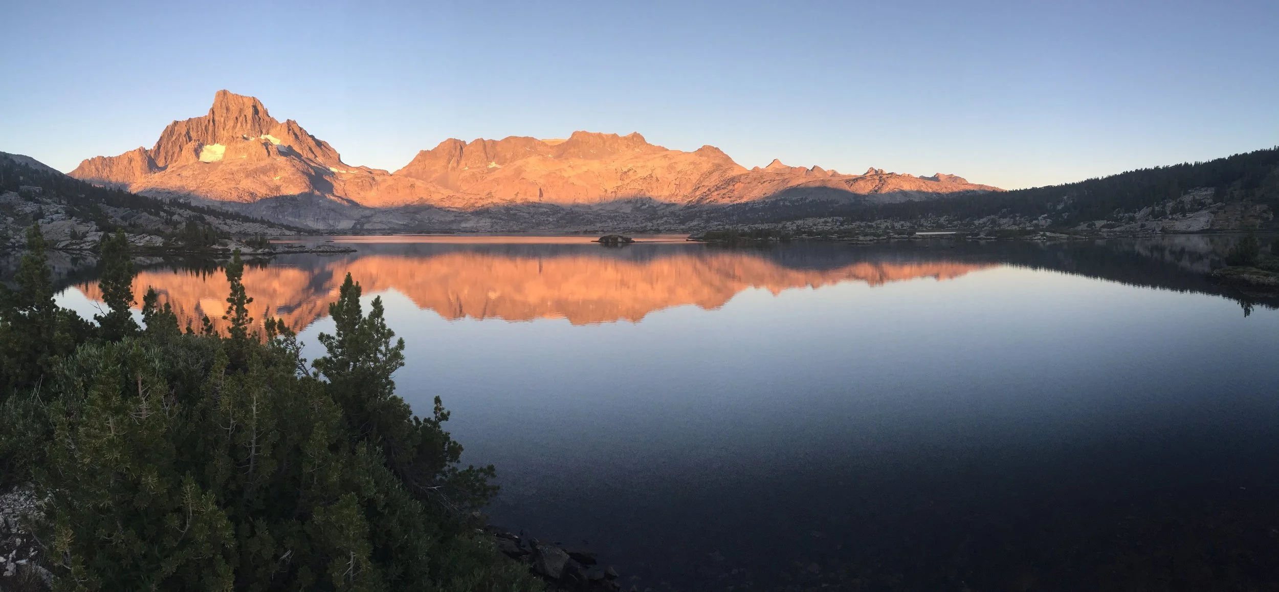 A mountain range reflecting in a calm lake with a clear sky.