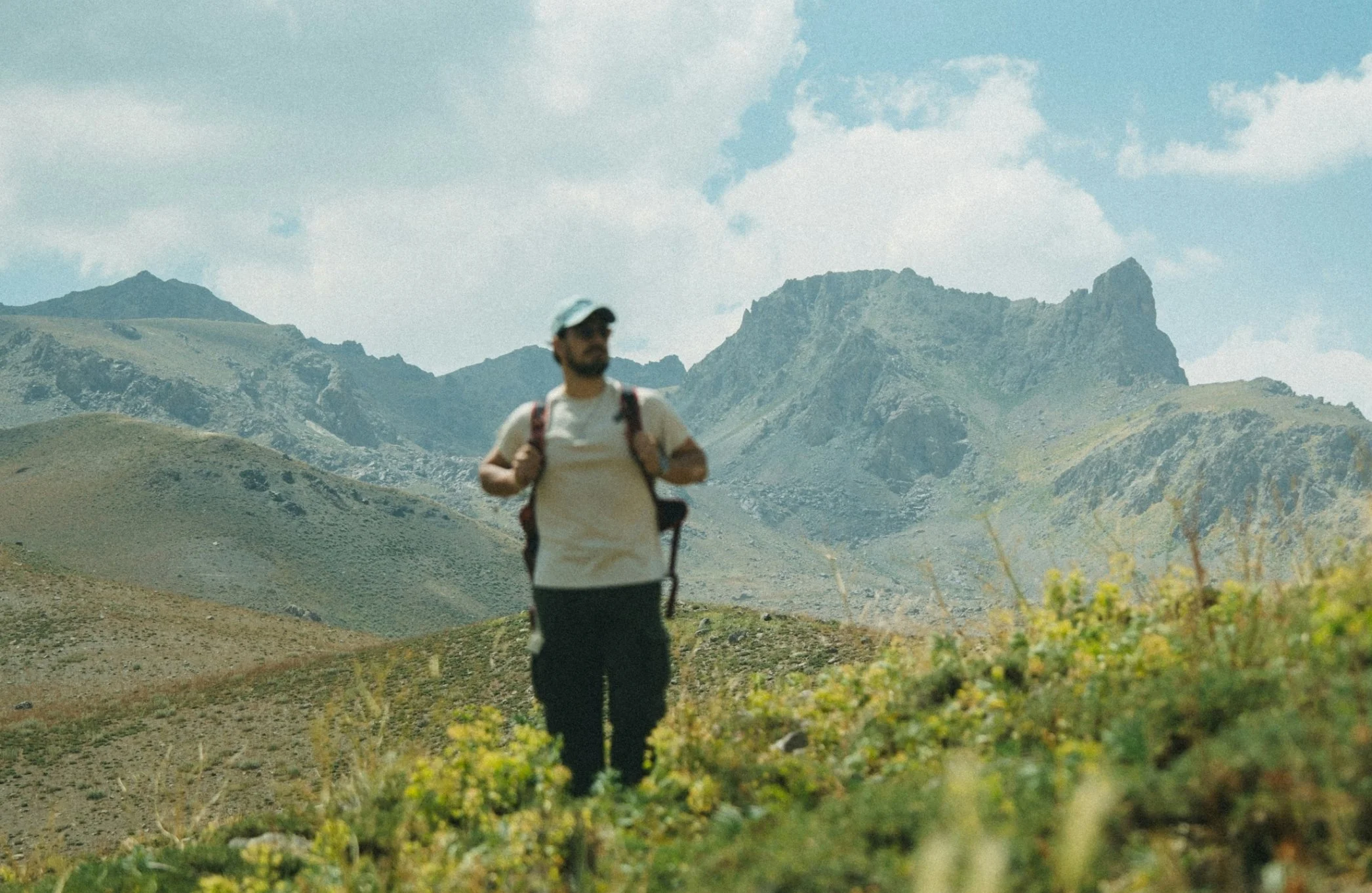 A man hiking in a mountainous area with rocky peaks under a blue sky with scattered clouds.